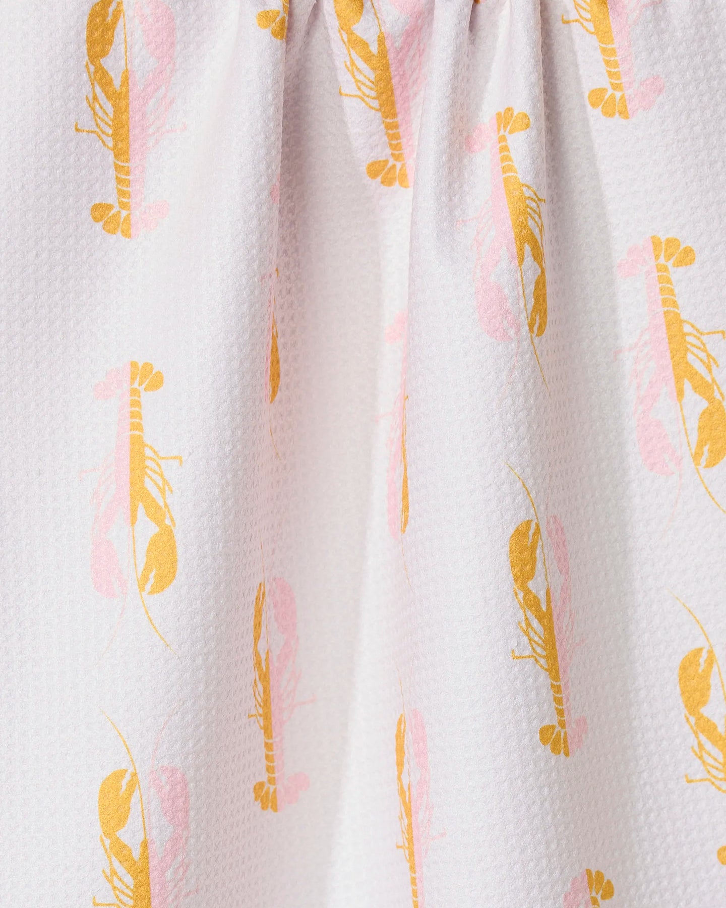 Close-up of GEOMETRYs Lobster Love kitchen towel, featuring a white textured fabric with an orange and pink lobster pattern. Made from recycled materials, the towel is gathered at the top to create gentle folds.