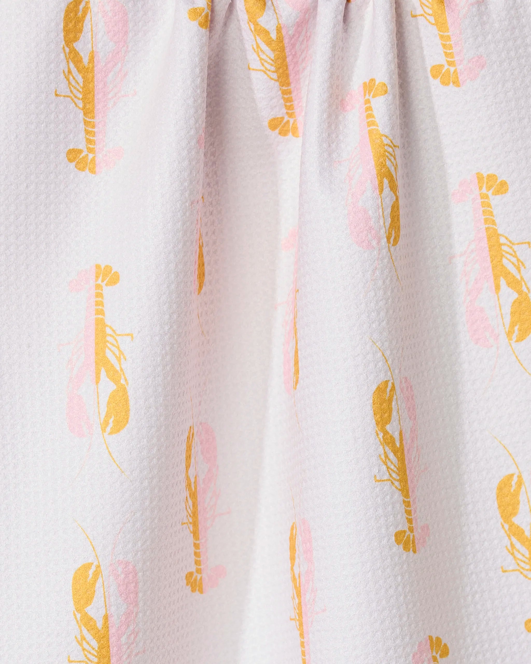 Close-up of GEOMETRYs Lobster Love kitchen towel, featuring a white textured fabric with an orange and pink lobster pattern. Made from recycled materials, the towel is gathered at the top to create gentle folds.