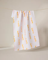 The GEOMETRY Lobster Love towel, made from recycled materials, features a white background with a yellow and pink abstract bird pattern and hangs on a clothesline against a neutral backdrop.