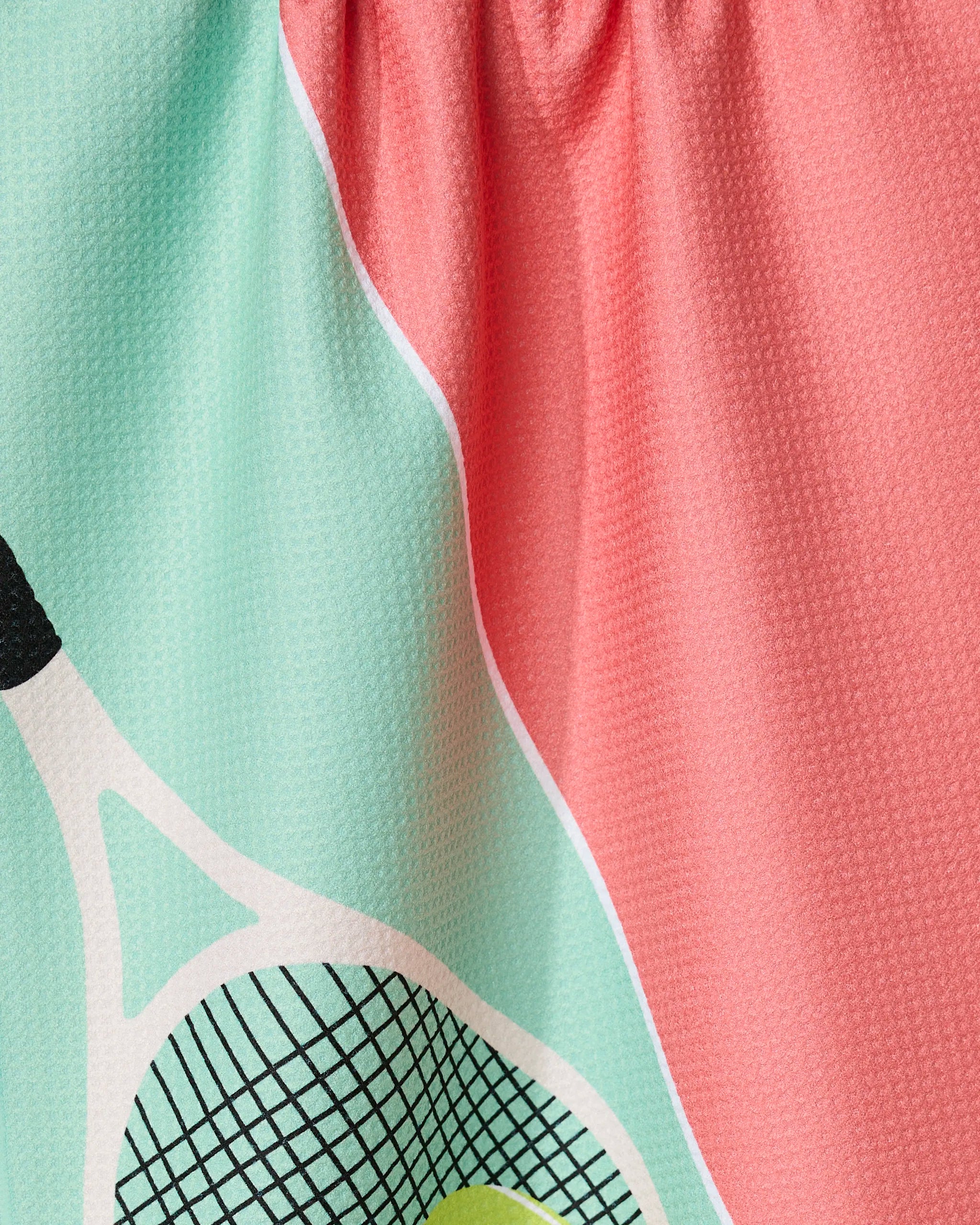 Close-up of GEOMETRYs Love 15 tea towel, featuring Geoweave fabric with a colorful tennis racket and ball design on mint green, paired with solid pink gathered fabric—vibrant and sustainably crafted from recycled materials.