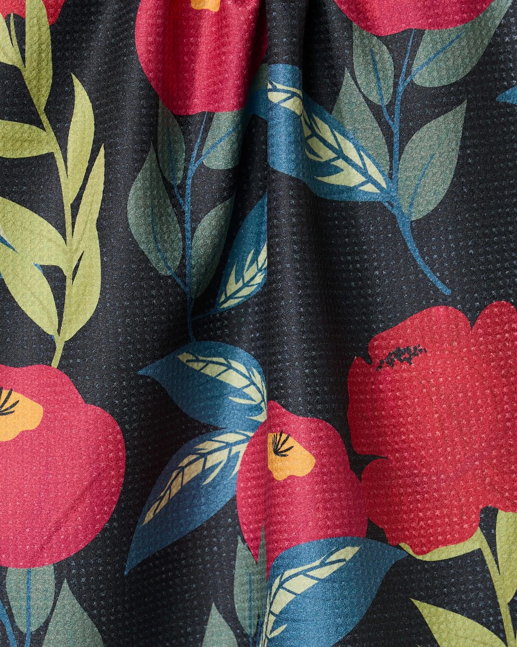 A close-up of GEOMETRY’s Lovely Night quick-drying towel, showcasing large red flowers and green leaves on a dark, subtly textured dotted background.