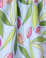 A close-up of the GEOMETRY May Flowers absorbent quick-dry towel, showcasing pink and peach tulip-style flowers with green leaves on a textured light blue background.