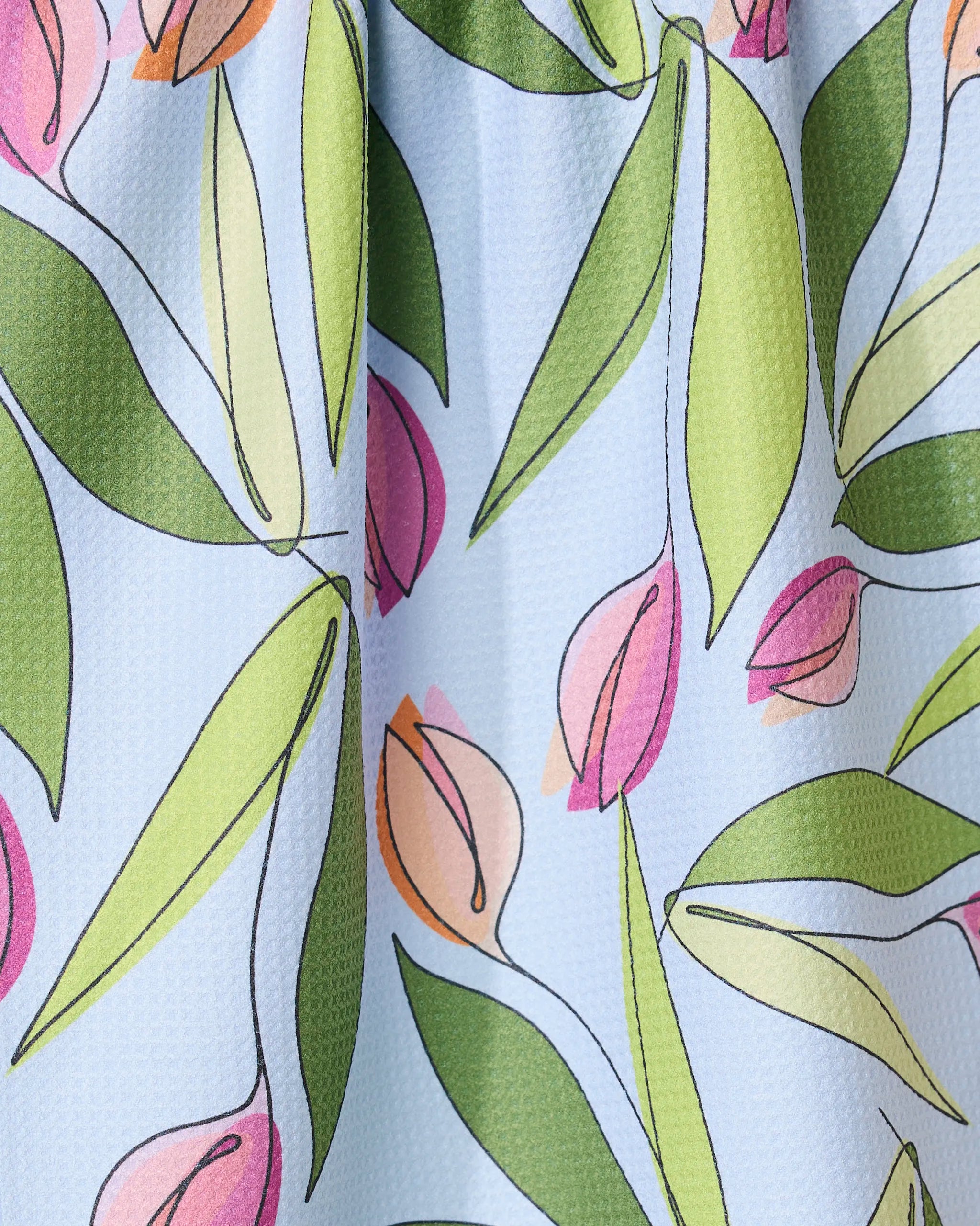 A close-up of the GEOMETRY May Flowers absorbent quick-dry towel, showcasing pink and peach tulip-style flowers with green leaves on a textured light blue background.