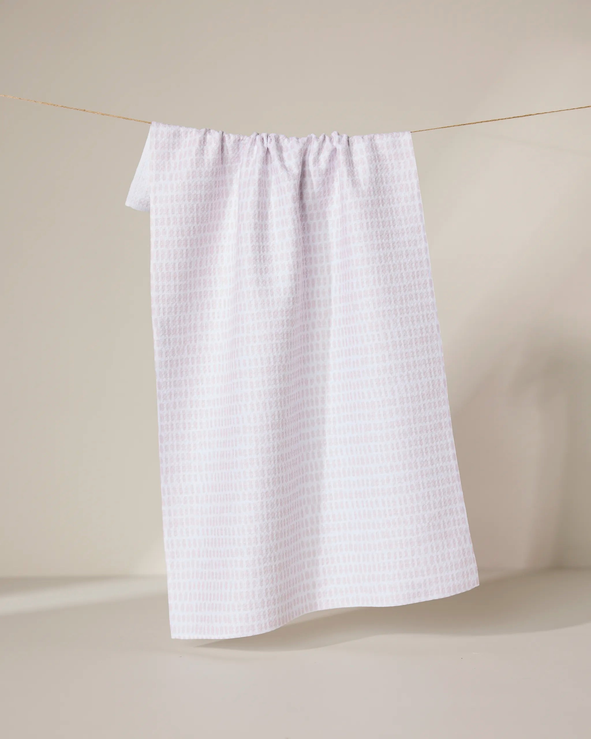 The Geometry Dot Dot Dot Blushed Bergamot towel, ultra-absorbent and white, hangs on a clothesline against a light beige background.