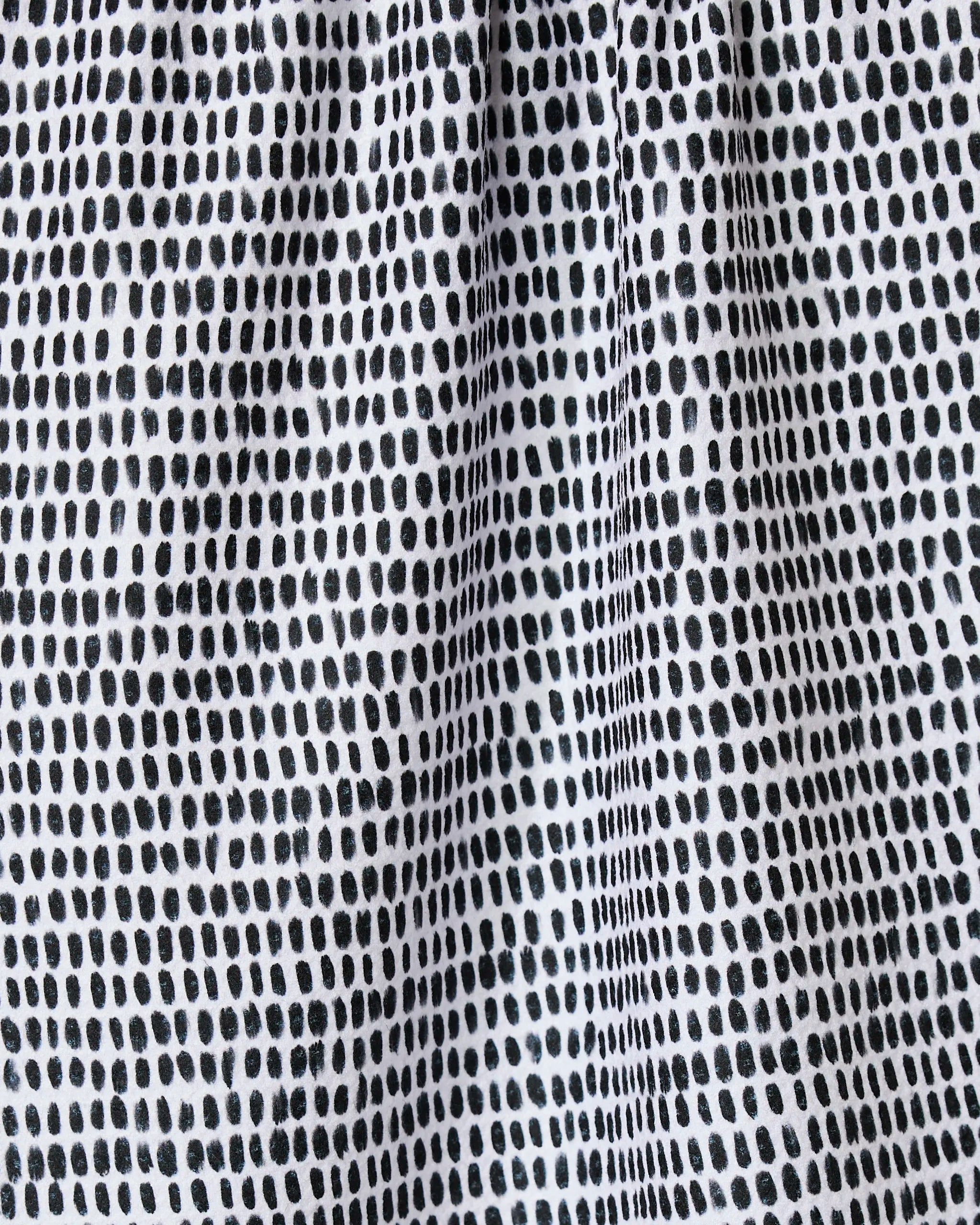 Close-up of Geometry’s Dot Dot Dot Fresh Linen kitchen towel, featuring a grid-like pattern of irregular black dots on white recycled fabric with a lightly gathered, textured look.
