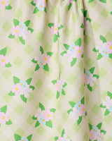 Close-up of GEOMETRYs Doting and Devoted kitchen tea towel, featuring a light green checkered pattern with white flowers, green leaves, and yellow-pink centers. Made from recycled materials with a quilted texture.