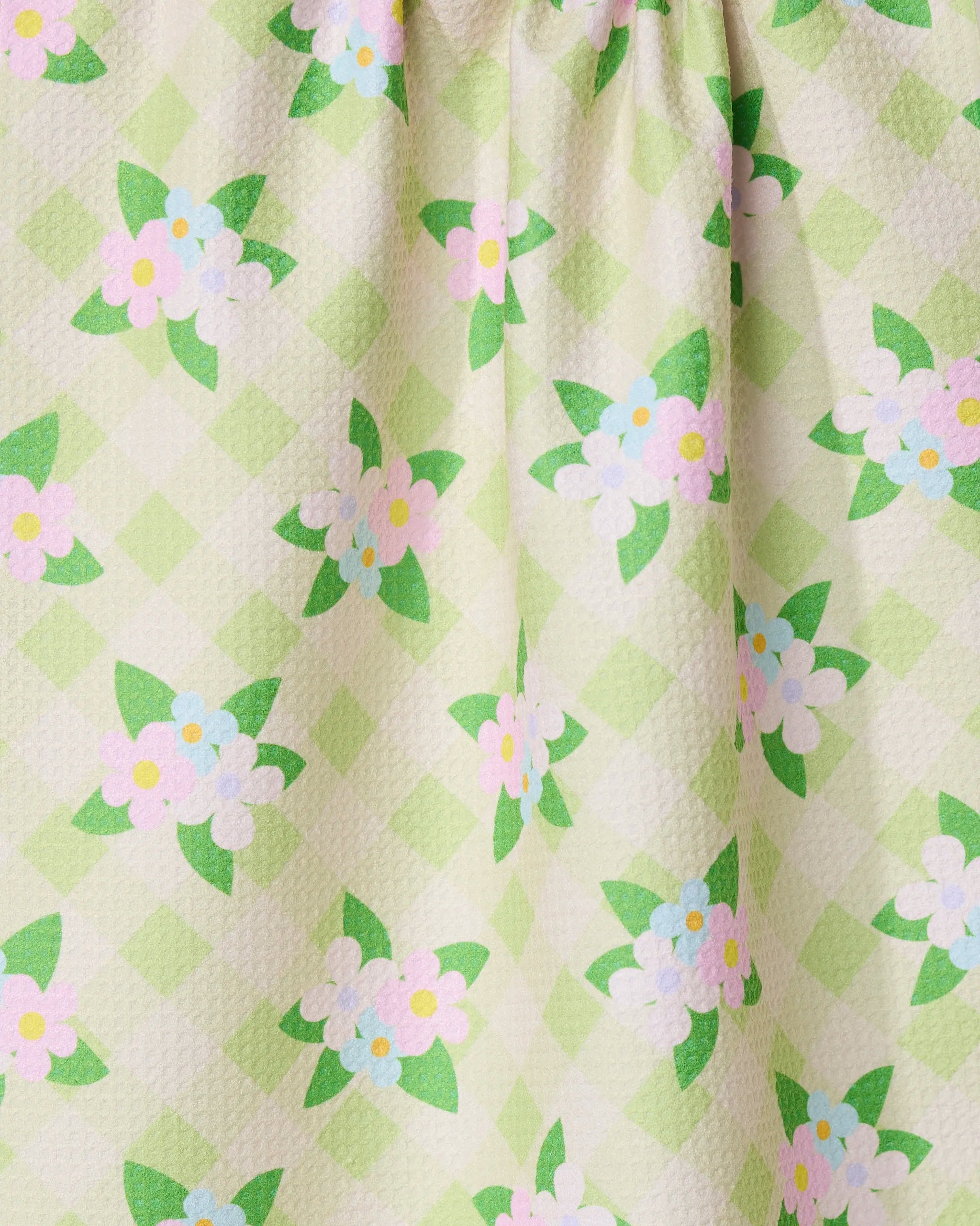 Close-up of GEOMETRYs Doting and Devoted kitchen tea towel, featuring a light green checkered pattern with white flowers, green leaves, and yellow-pink centers. Made from recycled materials with a quilted texture.
