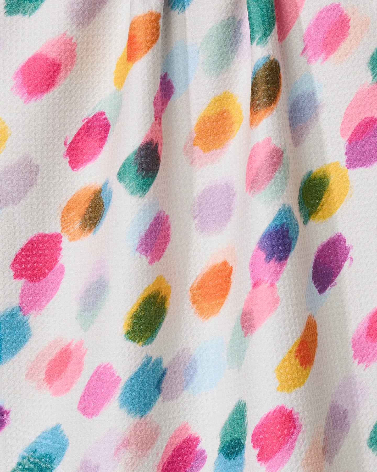 The Downpour tea towel by GEOMETRY features colorful, irregular paint-like dots in pink, blue, green, orange, yellow, and purple on a white textured surface made from recycled materials, with soft shadows from subtle fabric folds.