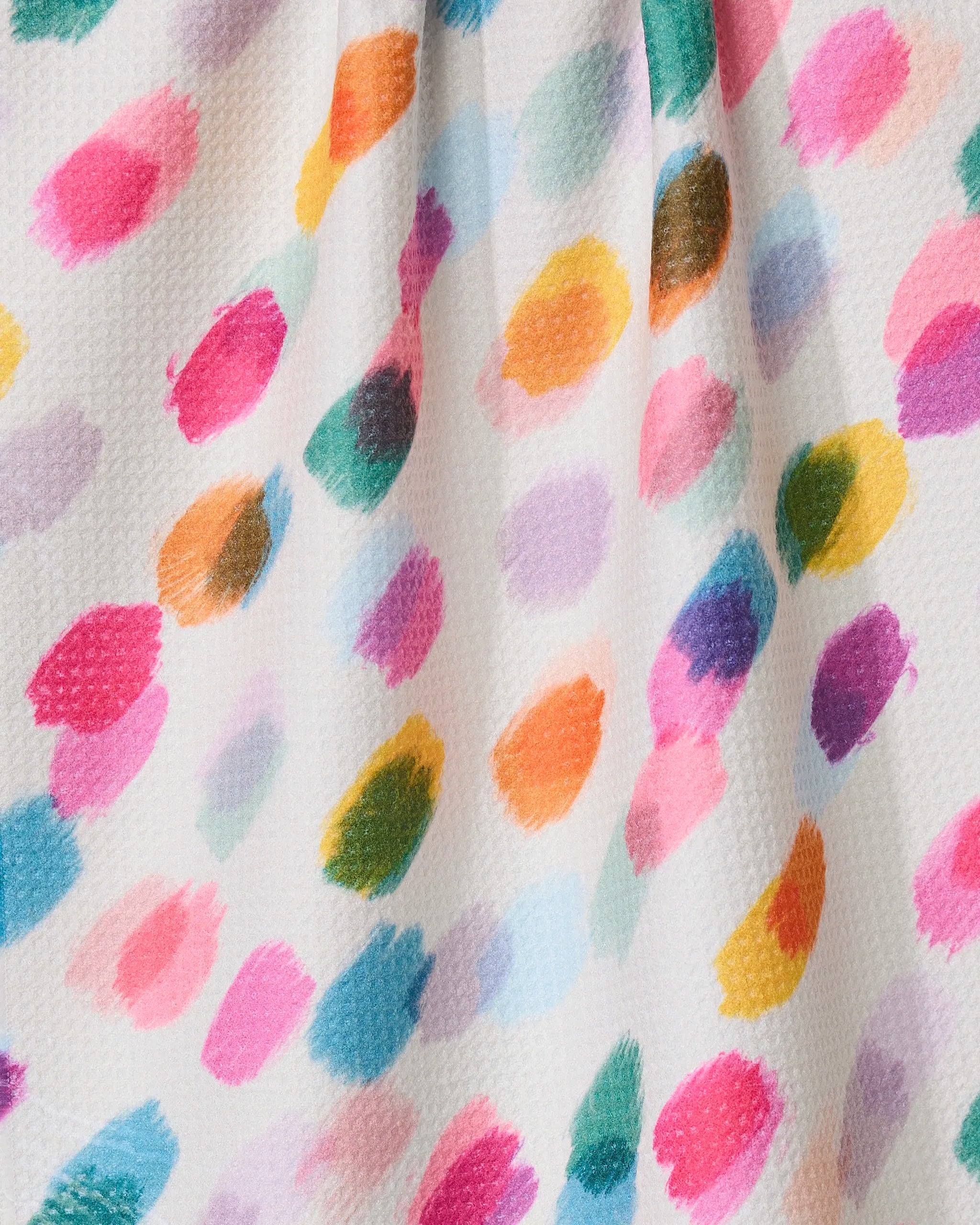 The Downpour tea towel by GEOMETRY features colorful, irregular paint-like dots in pink, blue, green, orange, yellow, and purple on a white textured surface made from recycled materials, with soft shadows from subtle fabric folds.