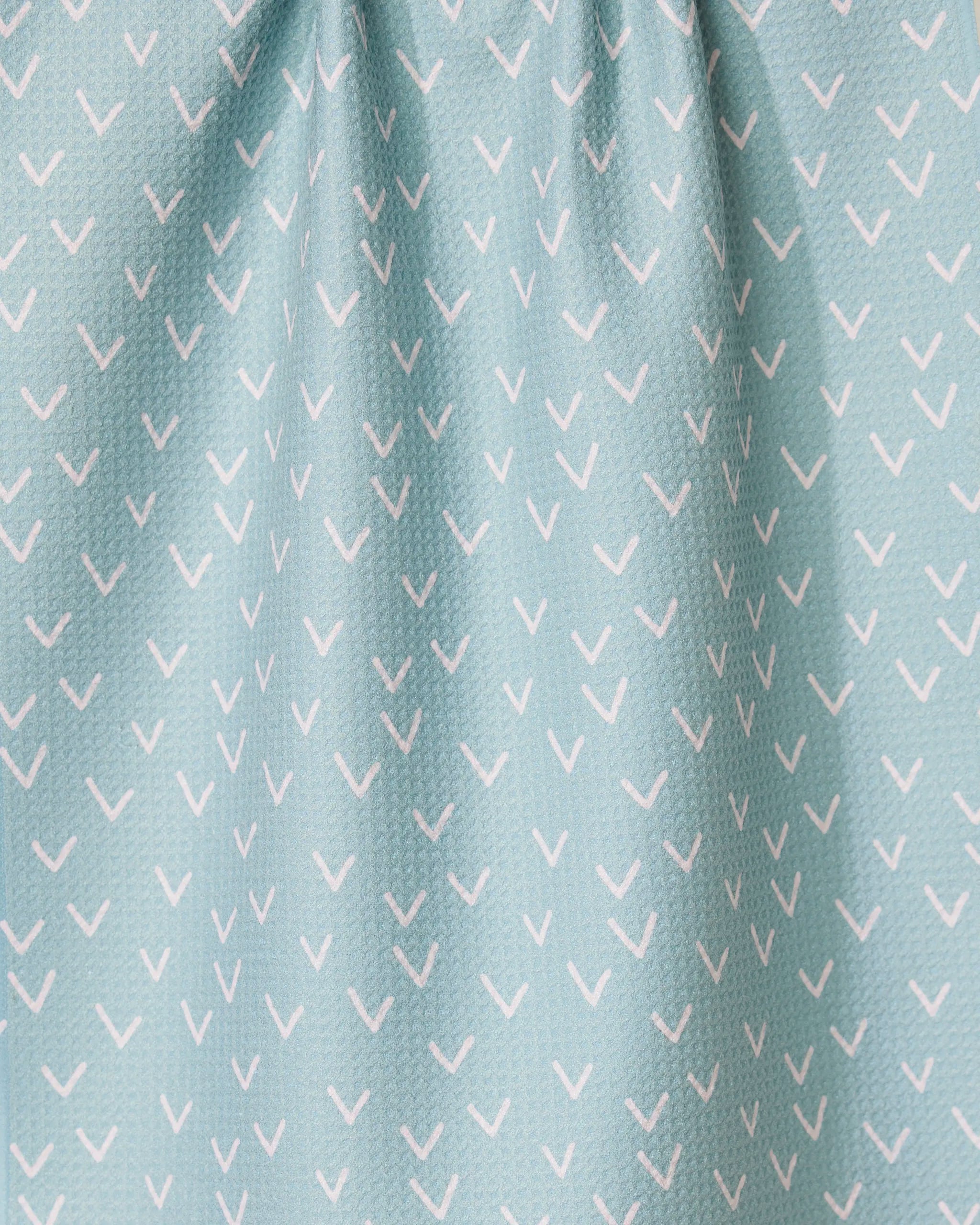 The Drawn Doves tea towel by GEOMETRY features a light blue color with small white check marks in diagonal rows, made from quick-drying fabric and gently gathered at the top.