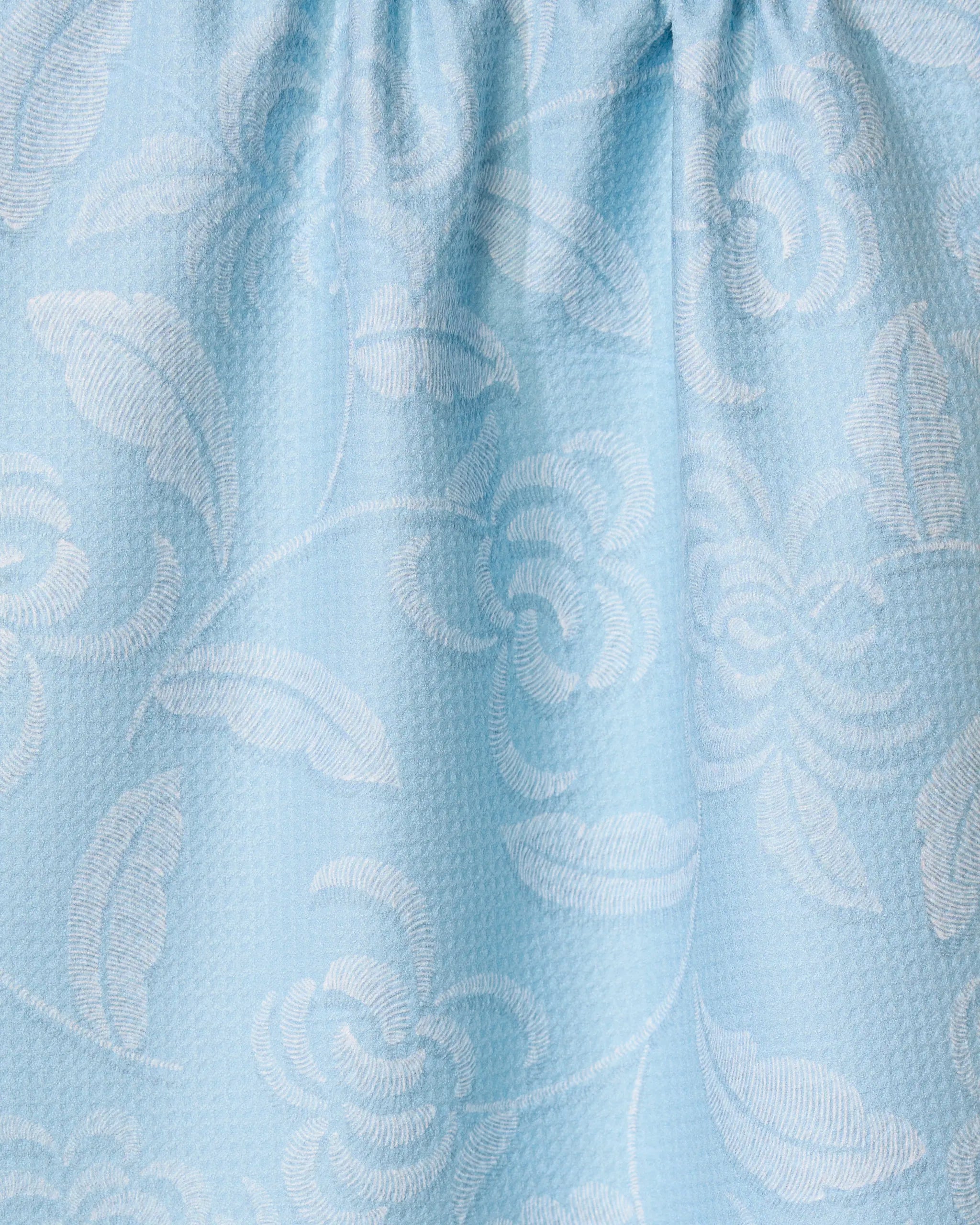 The Ediths Embroidery tea towel by GEOMETRY features a raised jacquard floral pattern in light blue, with shiny flowers and gentle gathers along the top—crafted from recycled materials for an elegant, eco-friendly touch.