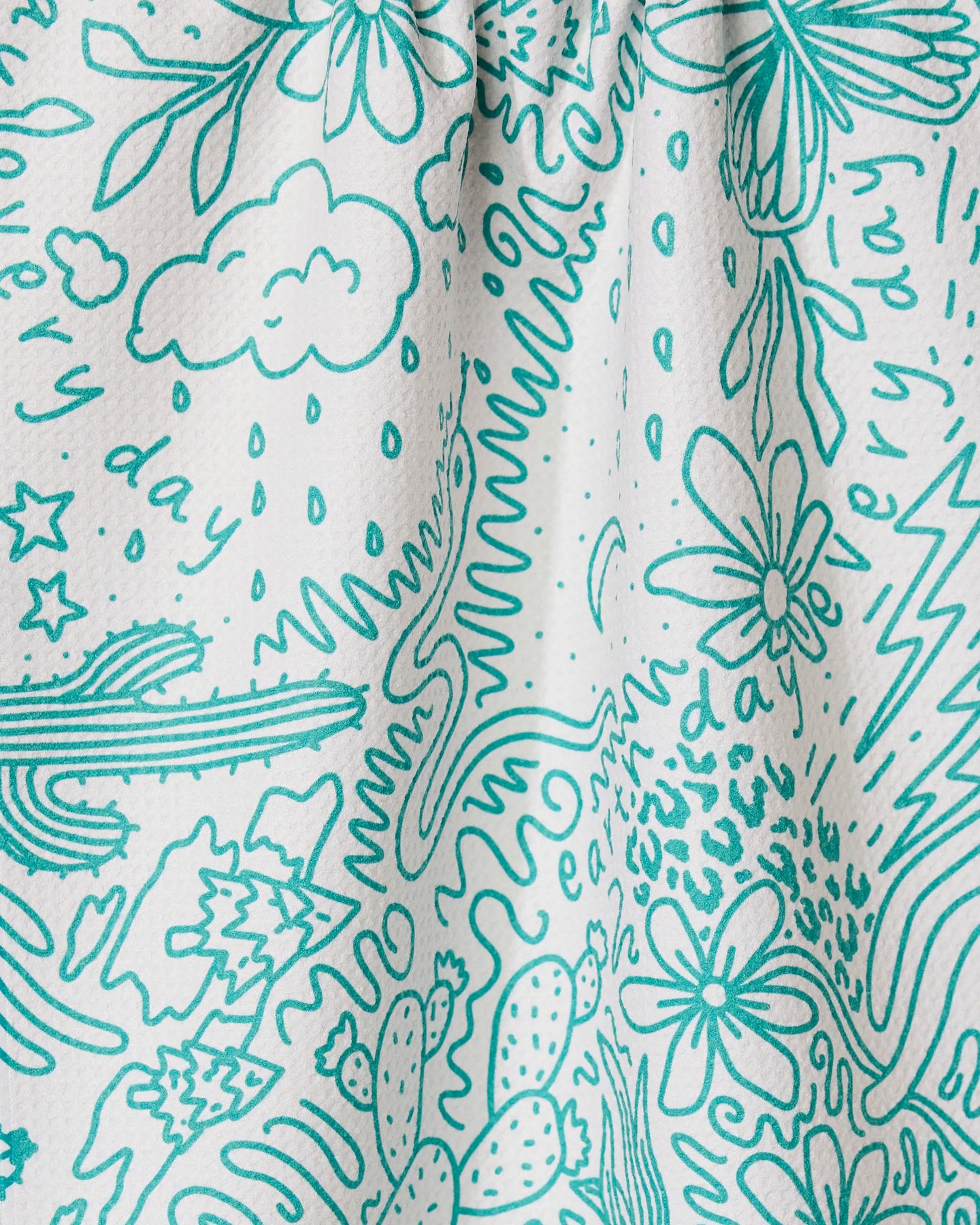The GEOMETRY Every Day tea towel features a white textured design with teal doodles—flowers, clouds, stars, rain, cacti, and squiggles—plus the phrase every day repeated across its ultra-absorbent surface.
