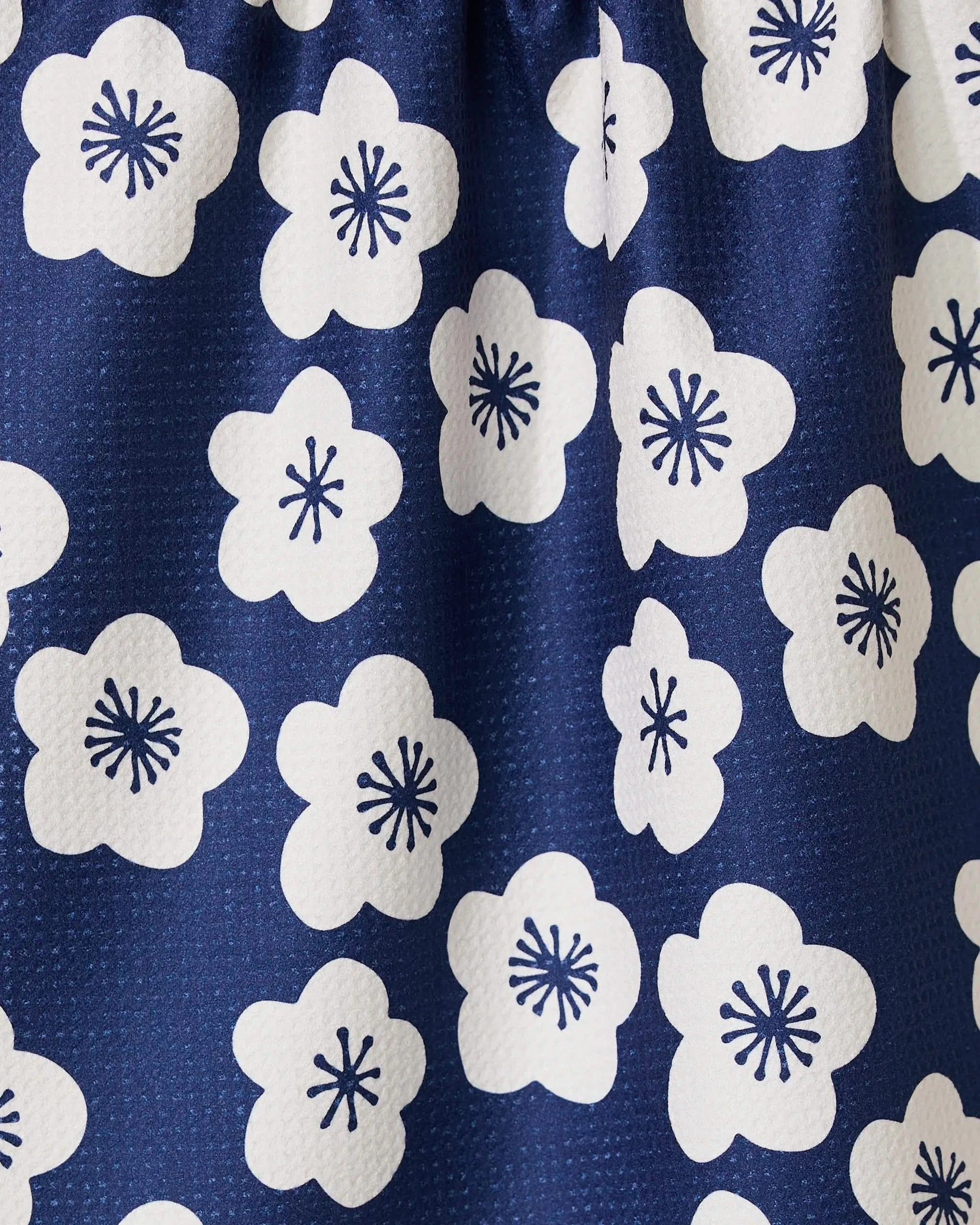 Close-up of Every Sunday by GEOMETRY: dark blue eco-friendly fabric with white five-petal flowers and navy starburst centers. Its dimpled, textured surface makes it an ideal choice for a stylish kitchen towel.