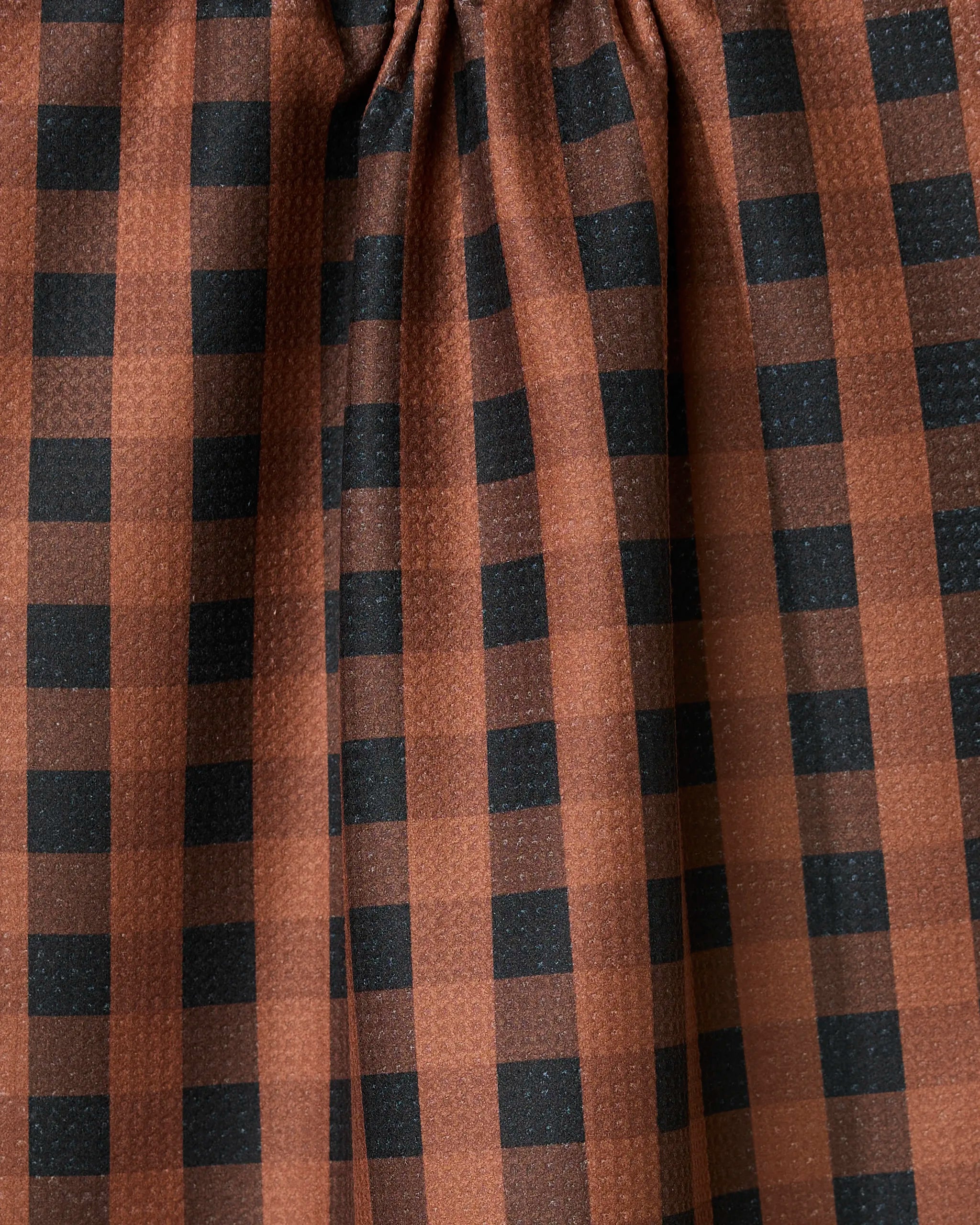 The Fall Gingham tea towel by GEOMETRY features brown fabric with a black checkered pattern and gentle gathers at the top, creating soft vertical folds—perfect as an ultra-absorbent addition to your kitchen.