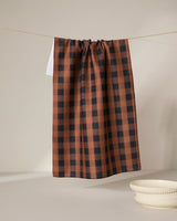 The GEOMETRY Fall Gingham tea towel hangs from a string against a plain light background, with two stacked cream-colored bowls placed nearby.