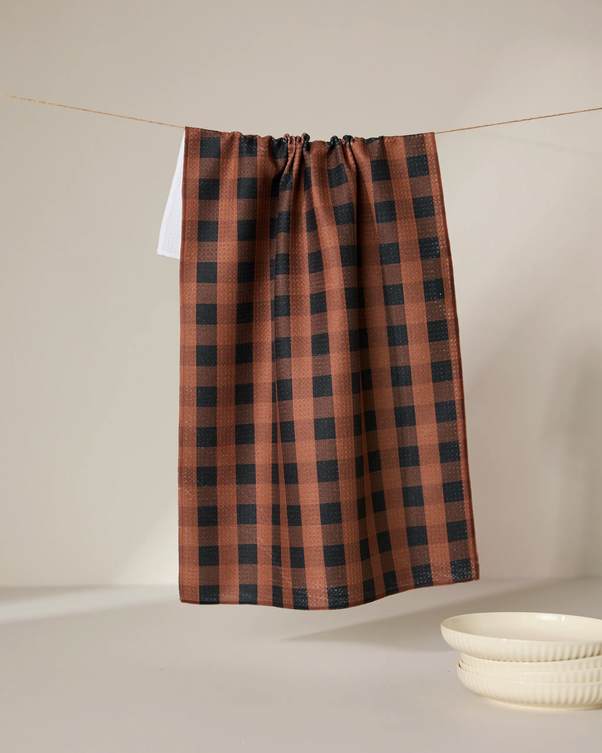 The GEOMETRY Fall Gingham tea towel hangs from a string against a plain light background, with two stacked cream-colored bowls placed nearby.
