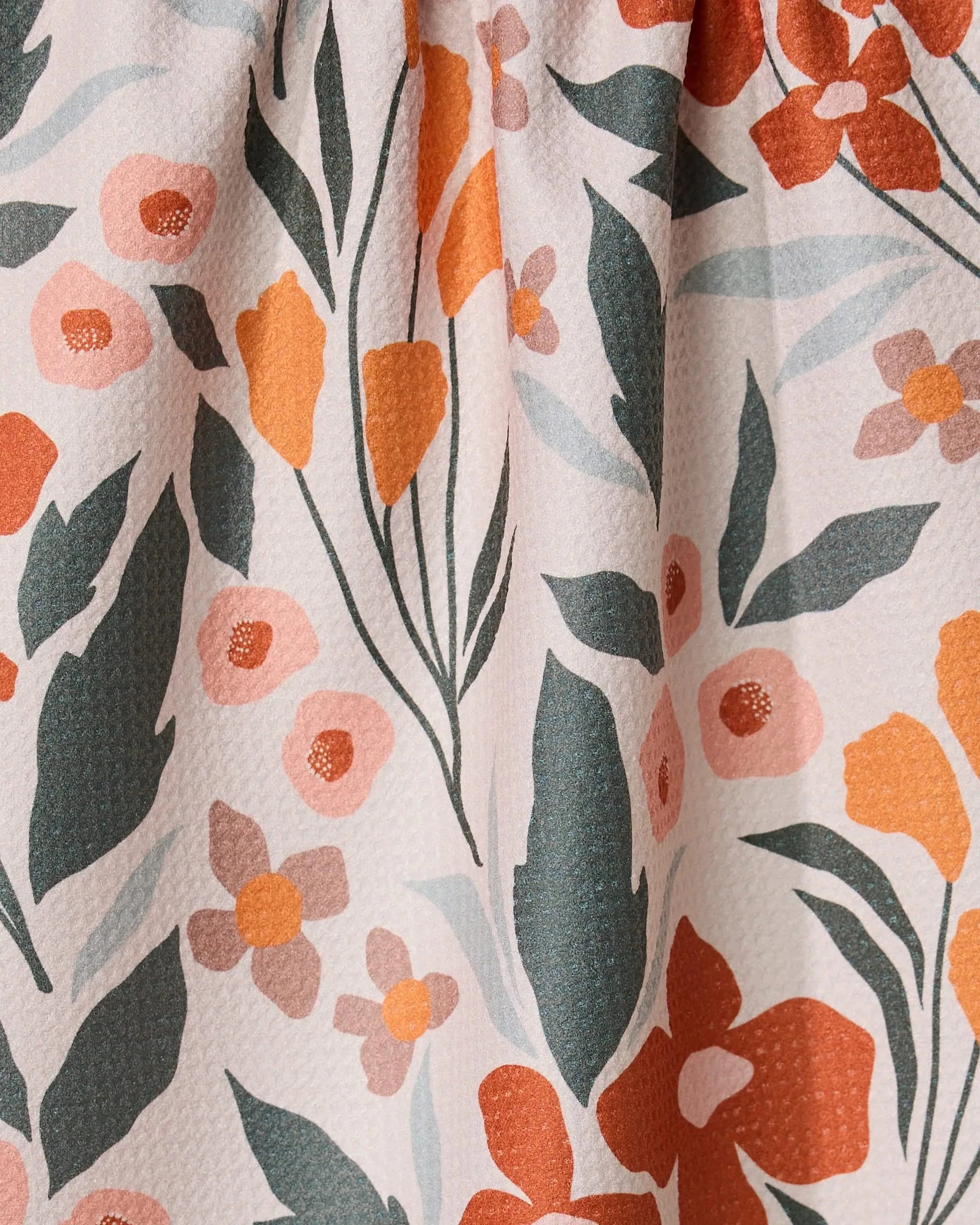A close-up of the GEOMETRY Fallowers tea towel, made from recycled materials with a floral pattern in orange, pink, and red flowers plus green leaves on a light beige, slightly textured fabric.