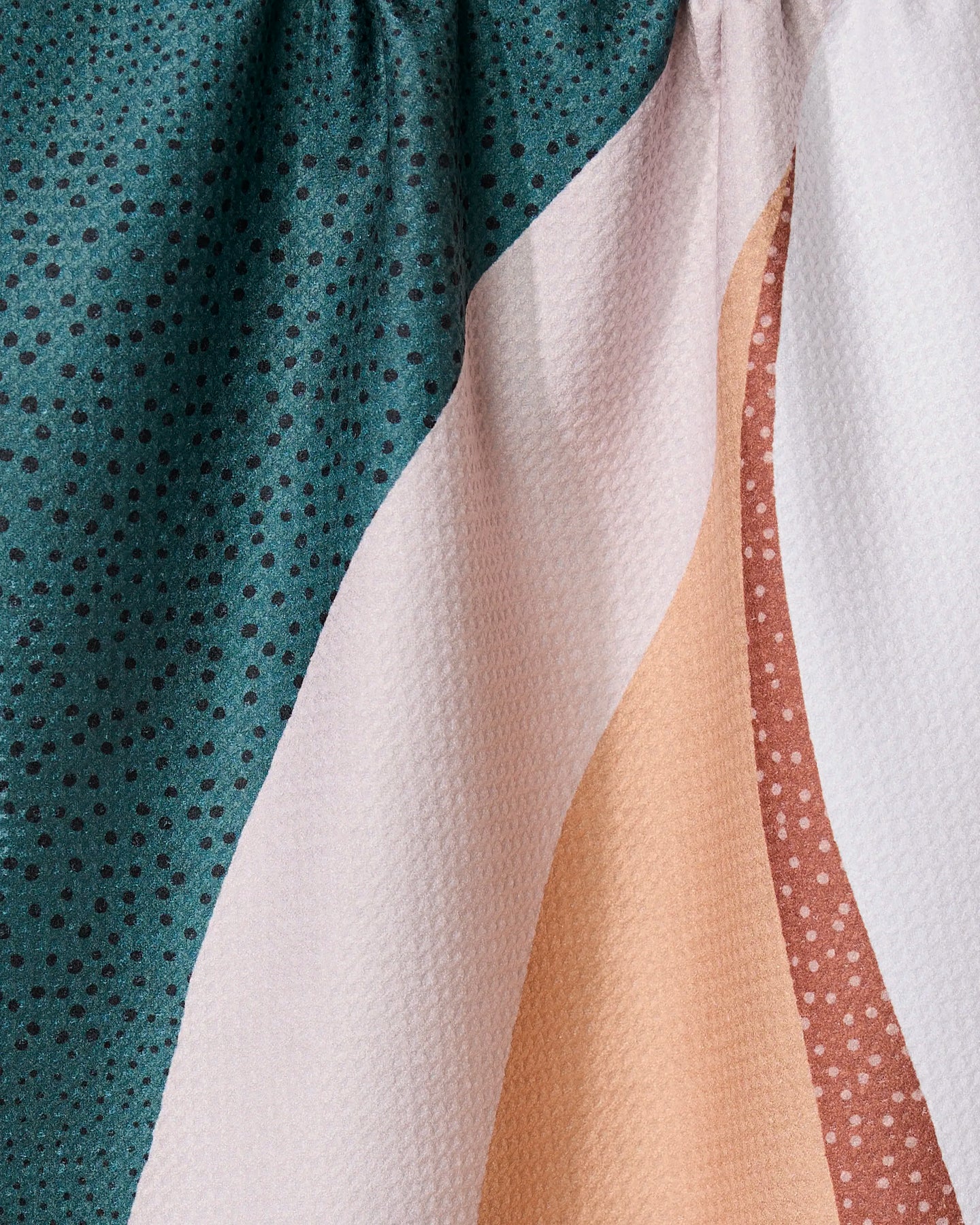 Close-up of the GEOMETRY Fan kitchen towel, showing abstract teal, white, peach, and pink geometric patterns with polka dots and textured folds—made from recycled materials.
