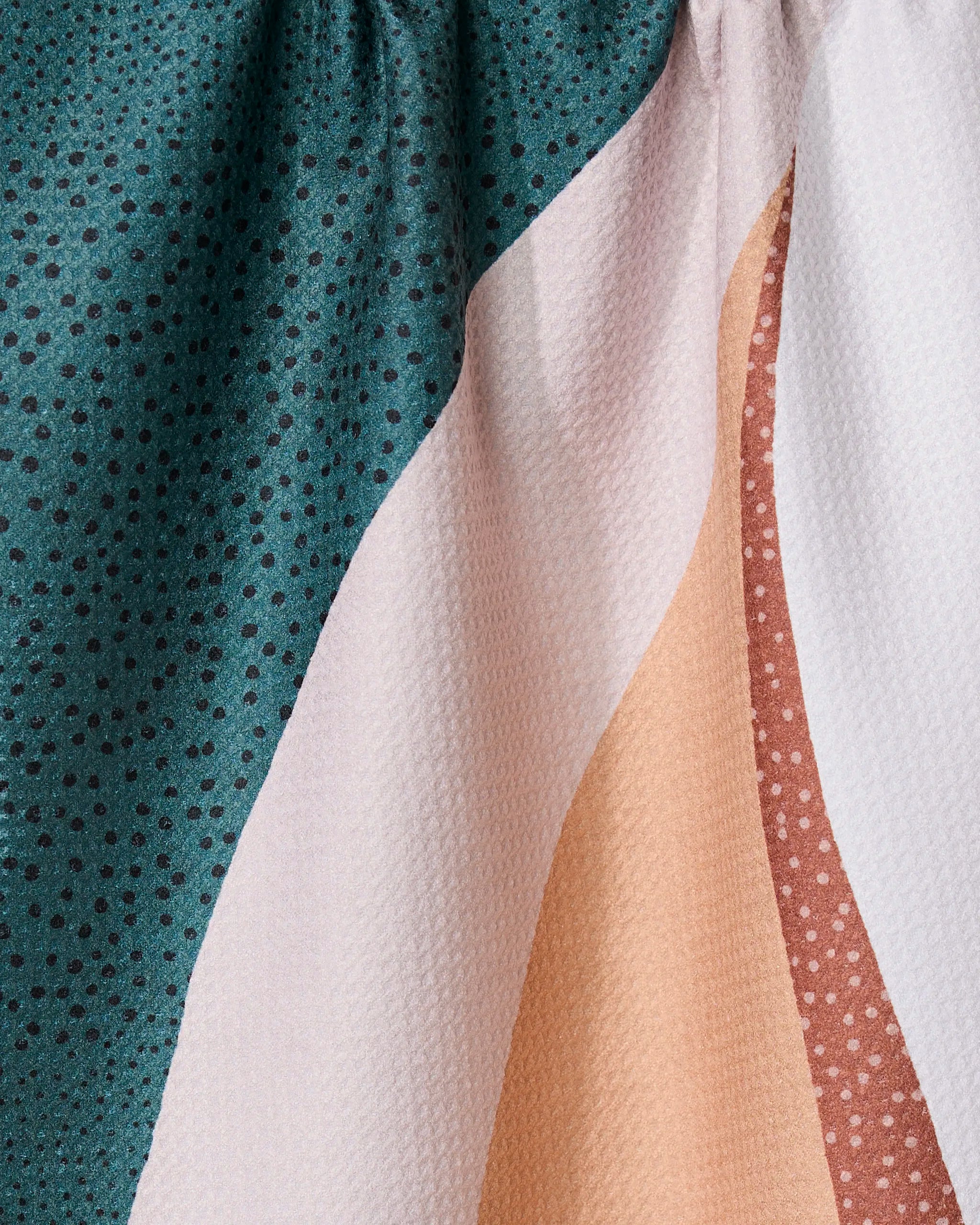 Close-up of the GEOMETRY Fan kitchen towel, showing abstract teal, white, peach, and pink geometric patterns with polka dots and textured folds—made from recycled materials.
