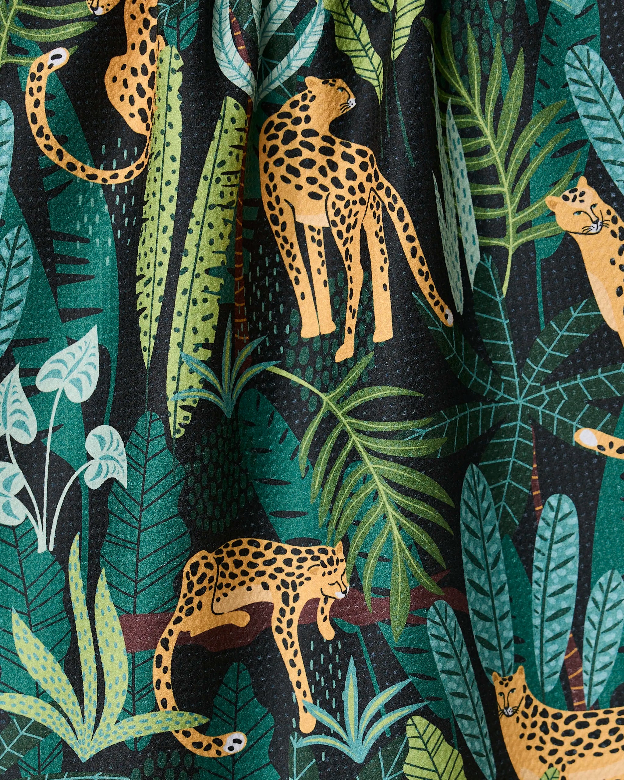 Feeling Spotty by GEOMETRY features leopards among lush green jungle leaves on a dark background. This vibrant tea towel adds a lively, tropical flair to your kitchen décor.