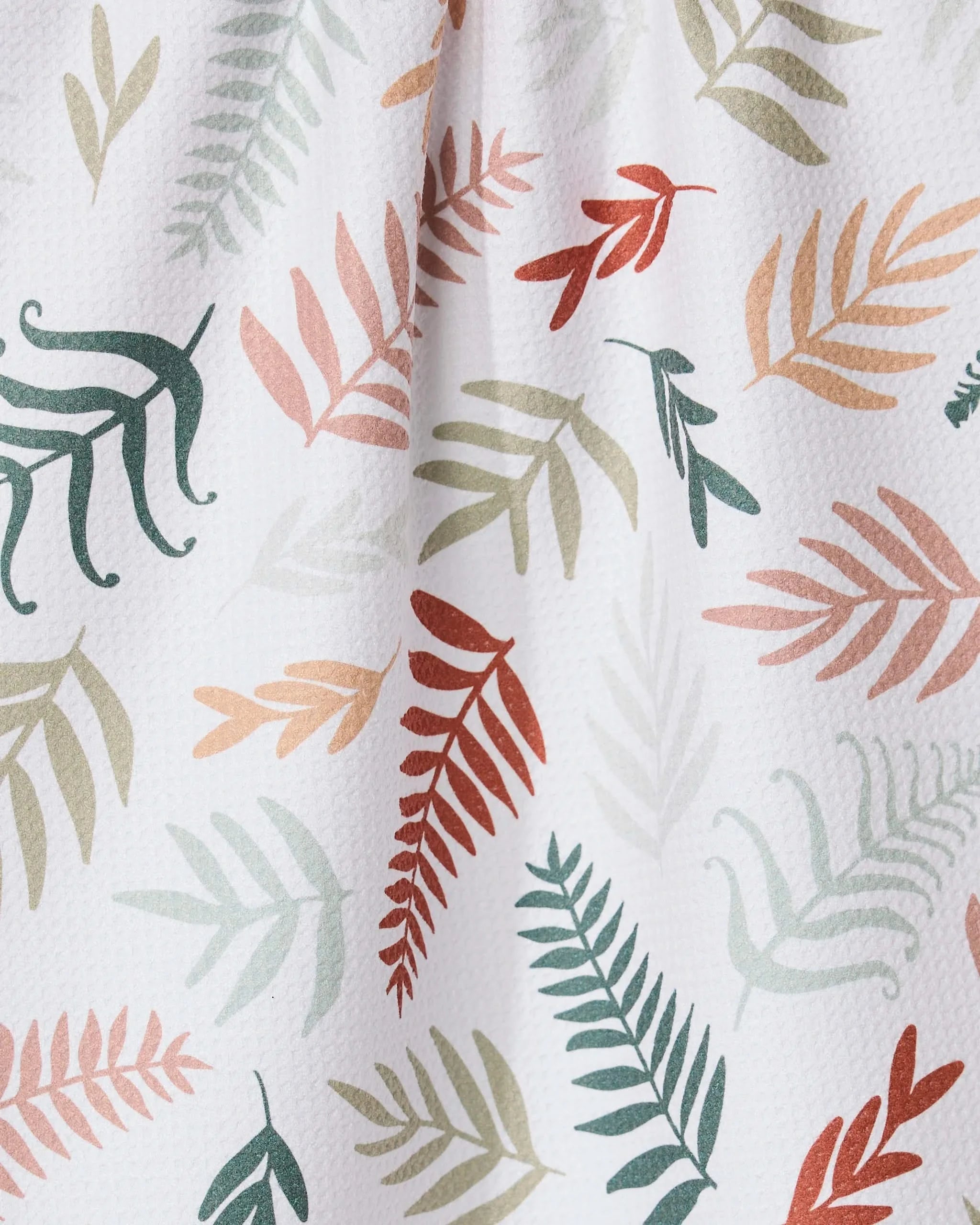 The GEOMETRY Forest Floor Ferns tea towel features a textured white fabric with colorful fern and leaf patterns in green, orange, peach, and yellow, crafted from recycled materials for ultra-absorbency and light folds.