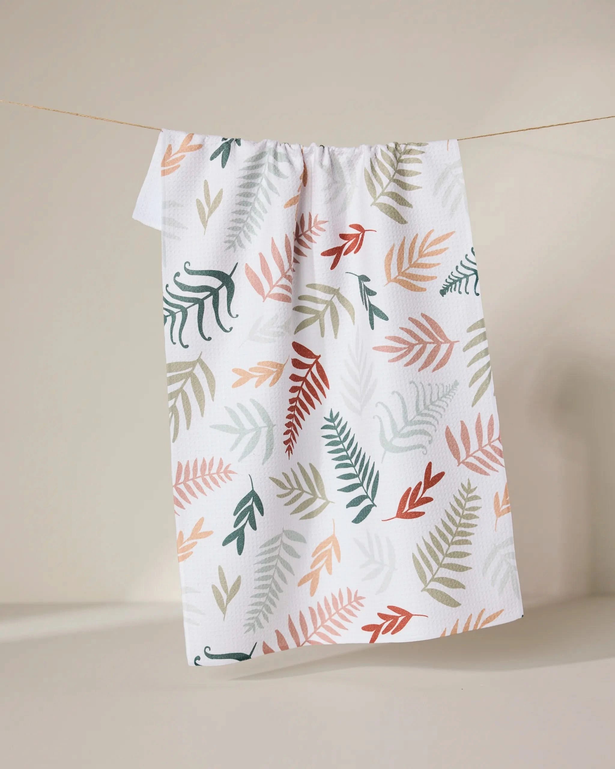 The Forest Floor Ferns tea towel by GEOMETRY features a vibrant leaf pattern in green, orange, pink, and beige on white. Made from ultra-absorbent recycled materials for both style and eco-friendly function. Hangs stylishly against any backdrop.