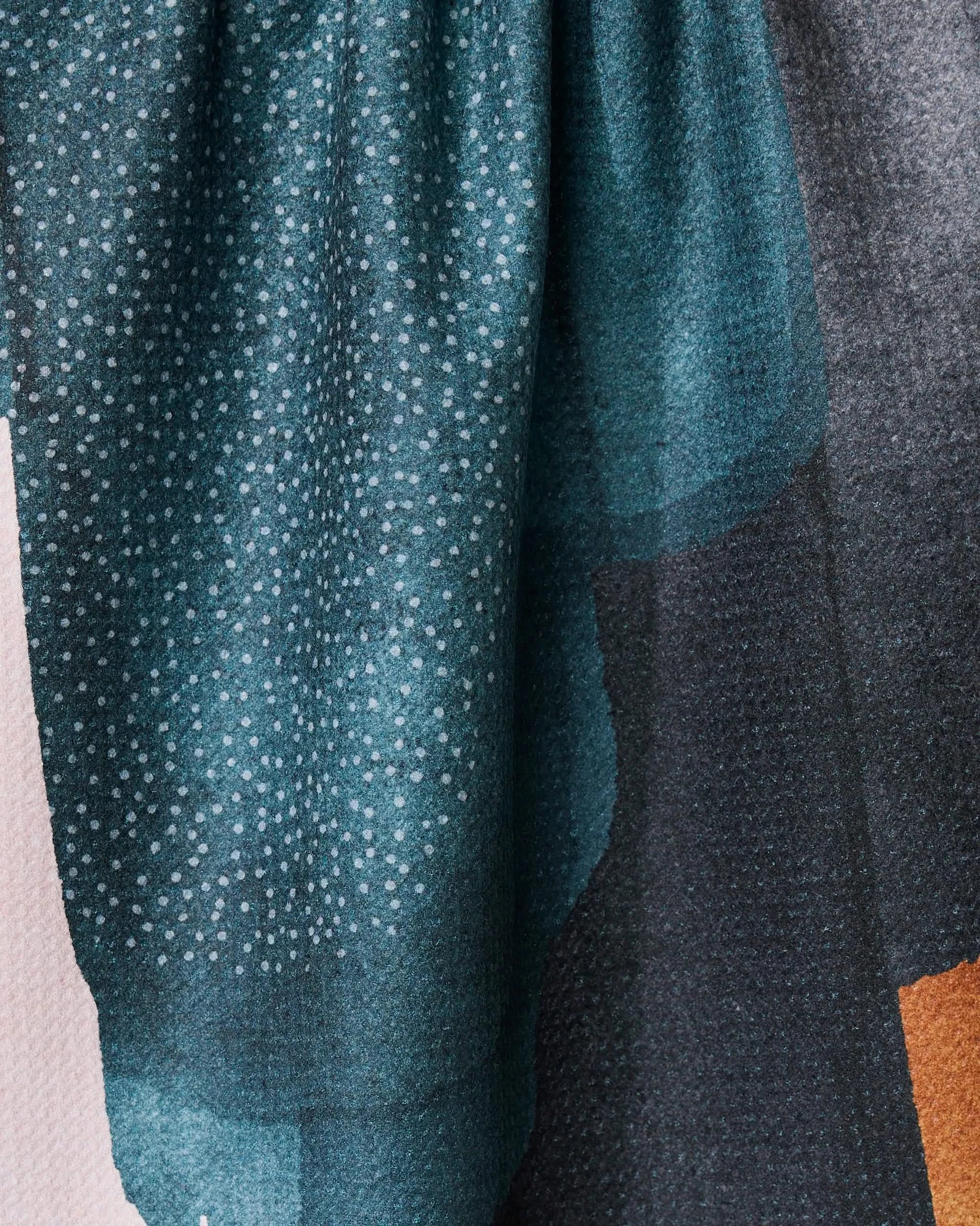 A close-up of GEOMETRY’s Founded fabric shows a teal and black gradient with small white dots and subtle folds, resembling a recycled kitchen towel, draped against a light background.