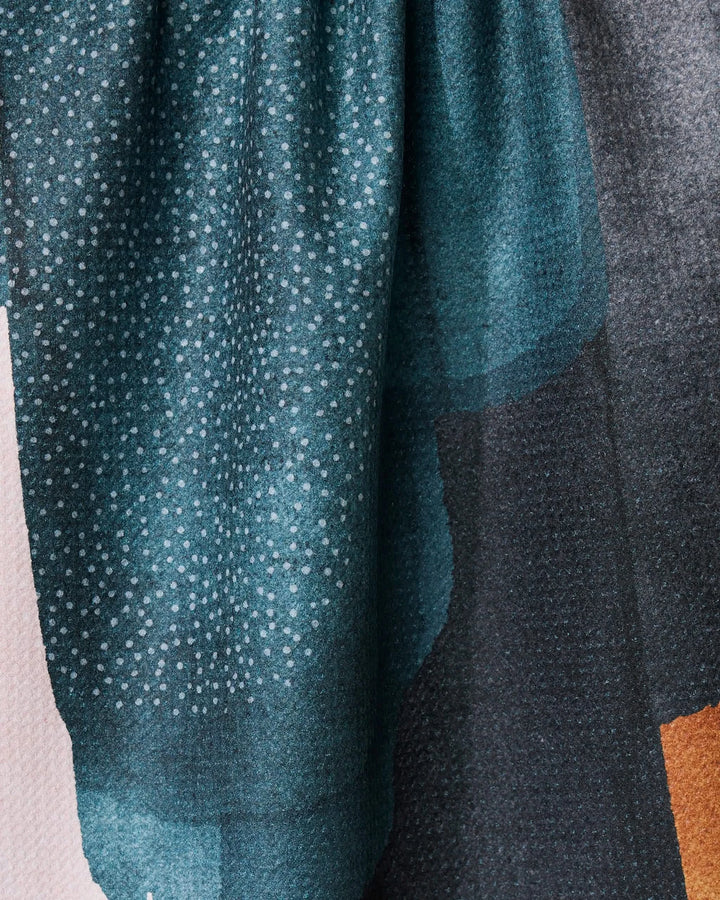 A close-up of GEOMETRY’s Founded fabric shows a teal and black gradient with small white dots and subtle folds, resembling a recycled kitchen towel, draped against a light background.