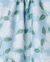The Garden Of Edith tea towel by GEOMETRY is light blue, made from quick-drying recycled materials, and features a textured surface printed with white hydrangea flowers and green leaves.