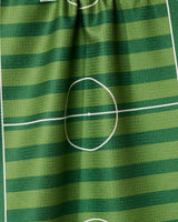 Close-up of GEOMETRYs Goal kitchen tea towel, made from recycled materials. It features green stripes and white soccer field markings, like the center circle and half-line. The ultra-absorbent towel has a slightly wrinkled texture.