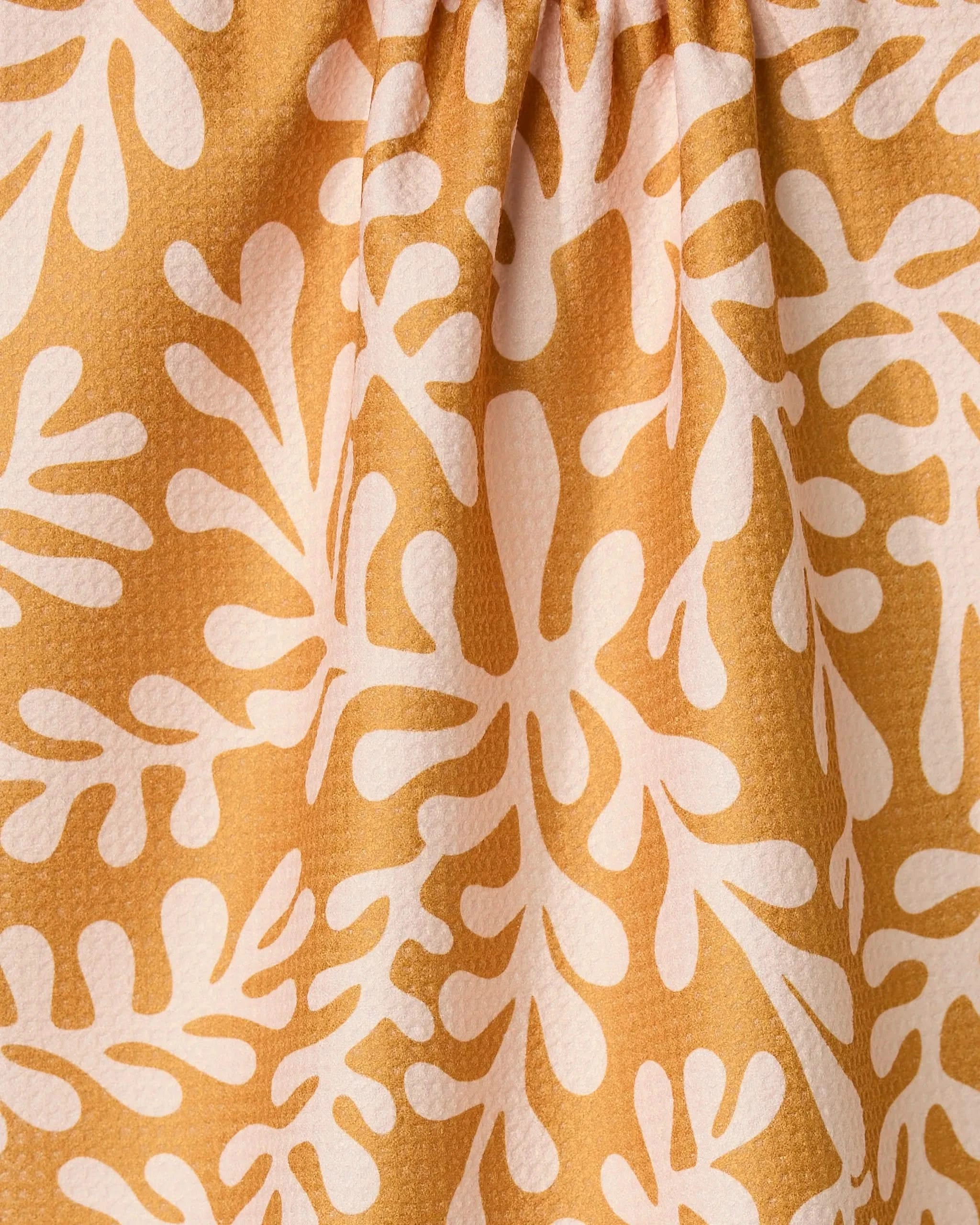 The Golden Fall tea towel by GEOMETRY features a yellow-orange, textured surface with an abstract white leaf pattern. Made from recycled materials, its quick-drying fabric creates soft folds and is slightly gathered at the top.