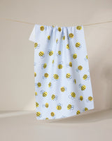 The GEOMETRY Buzzing tea towel, in light blue with a playful yellow and black bumblebee pattern, hangs on a string against a plain, light background.