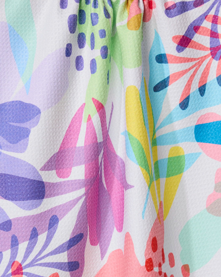 Close-up of GEOMETRYs Botanical Burst kitchen towel, showcasing colorful abstract floral patterns with pink, purple, blue, green, and yellow shapes on textured white recycled fabric.