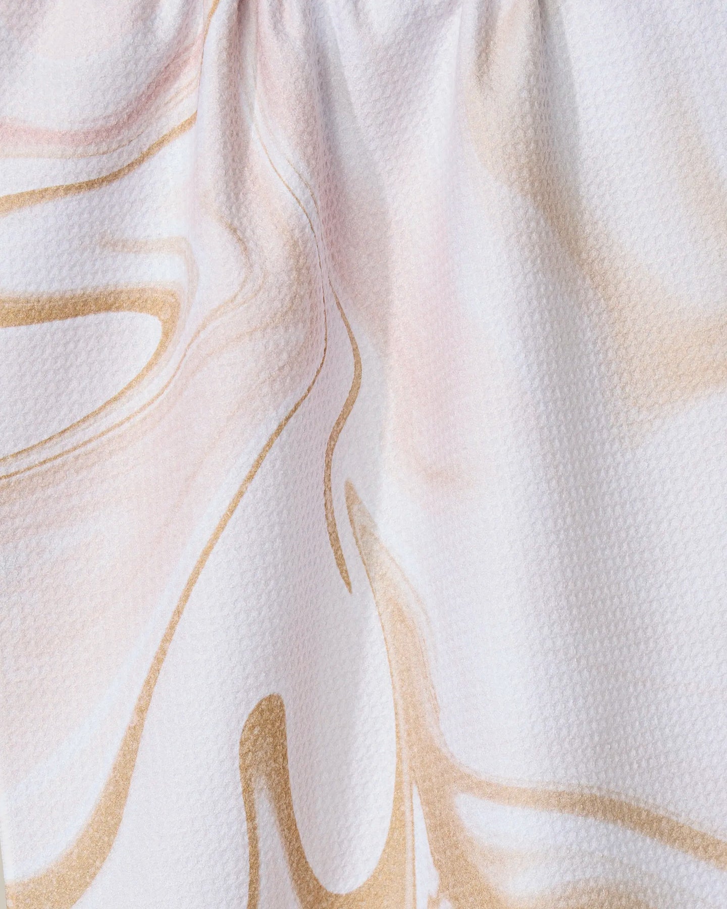 Close-up of GEOMETRYs Vanilla tea towel, crafted from recycled materials with a soft abstract marble pattern in beige and light pink on a white textured background. The top of the fabric is slightly gathered.