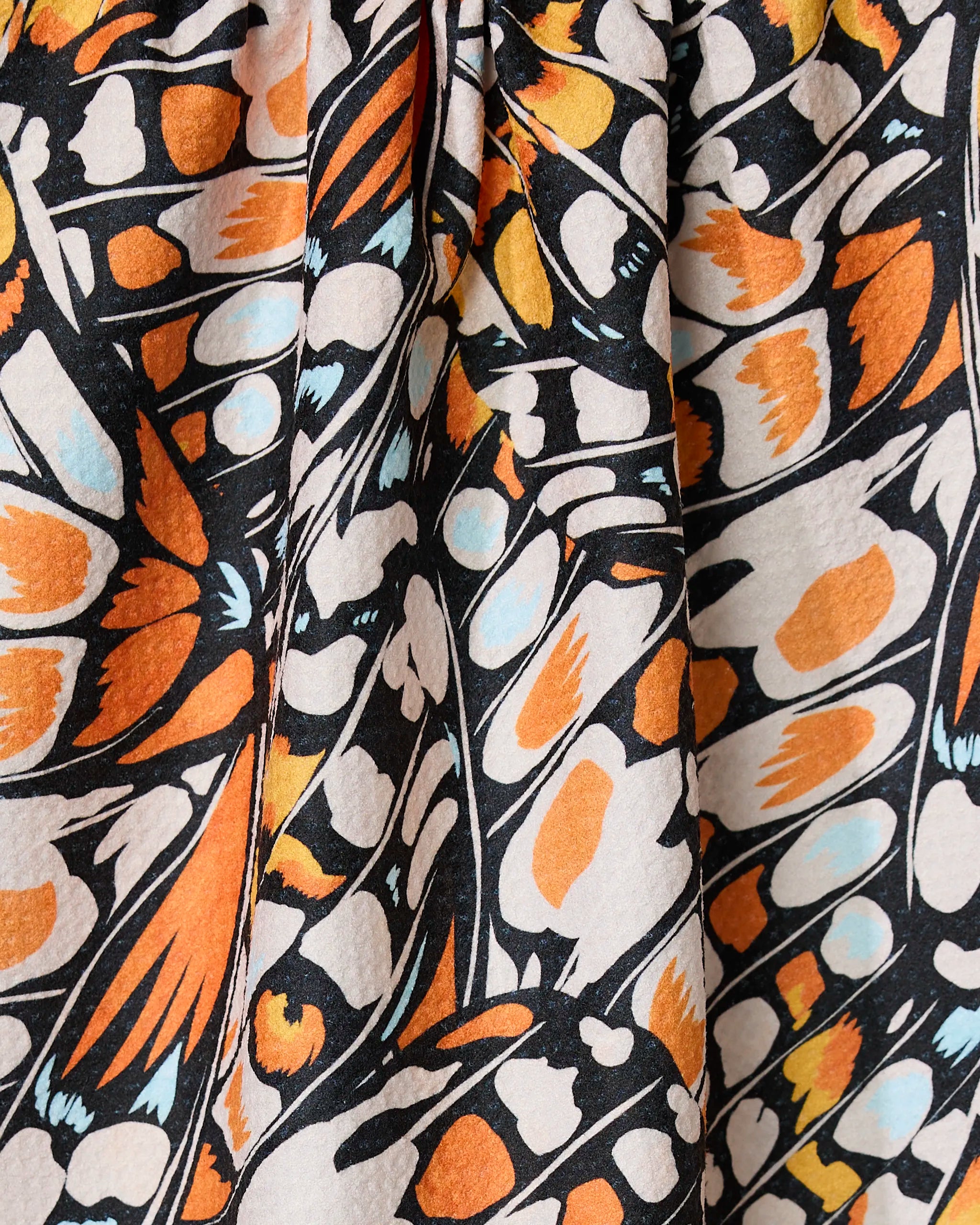 Wings in the Wind by GEOMETRY is a quick-drying towel with an abstract butterfly wing pattern—black outlines frame orange, white, and light blue shapes. Slight gathering adds texture and vibrant color to this eye-catching design.