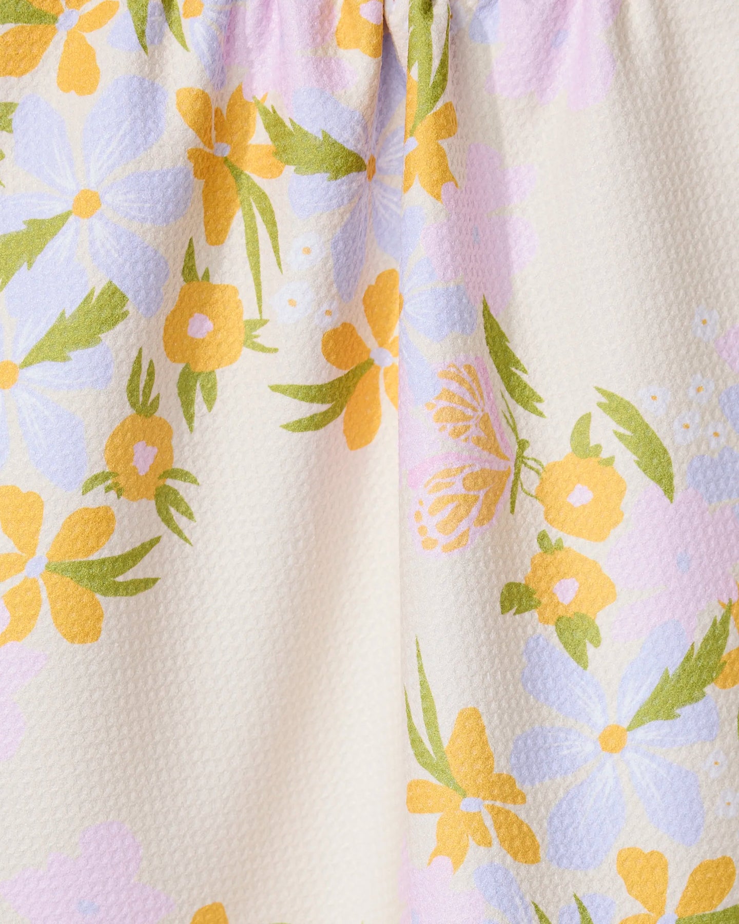 The GEOMETRY Abloom kitchen towel features a close-up of absorbent, slightly textured fabric with a pastel floral pattern—yellow, white, and purple flowers with green leaves on a light beige background.