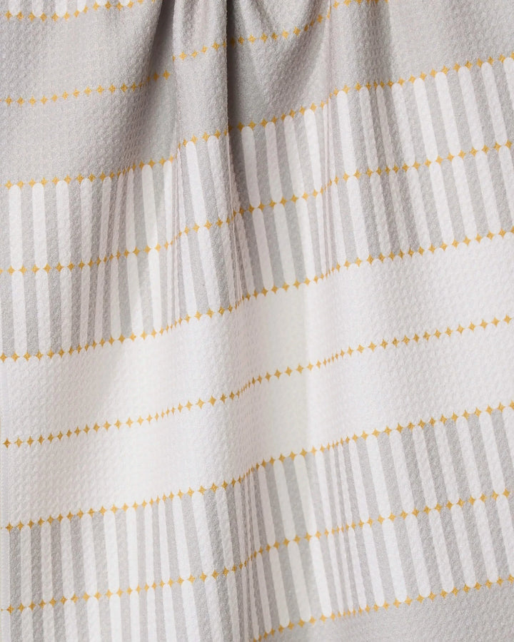 A close-up of the GEOMETRY Bâton Dor absorbent dish towel, featuring horizontal light gray stripes and dotted yellow lines on a textured white background, with gentle fabric folds at the top.