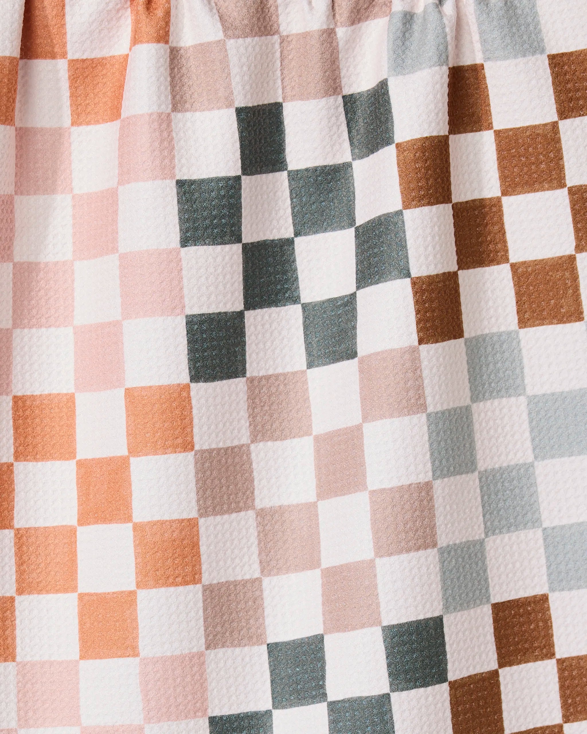 A close-up of the GEOMETRY Autumn Checkers towel shows its ultra-absorbent, crinkled fabric with a checkered pattern in muted pink, brown, gray, and white. Even lighting highlights the unique texture and evenly spaced squares.