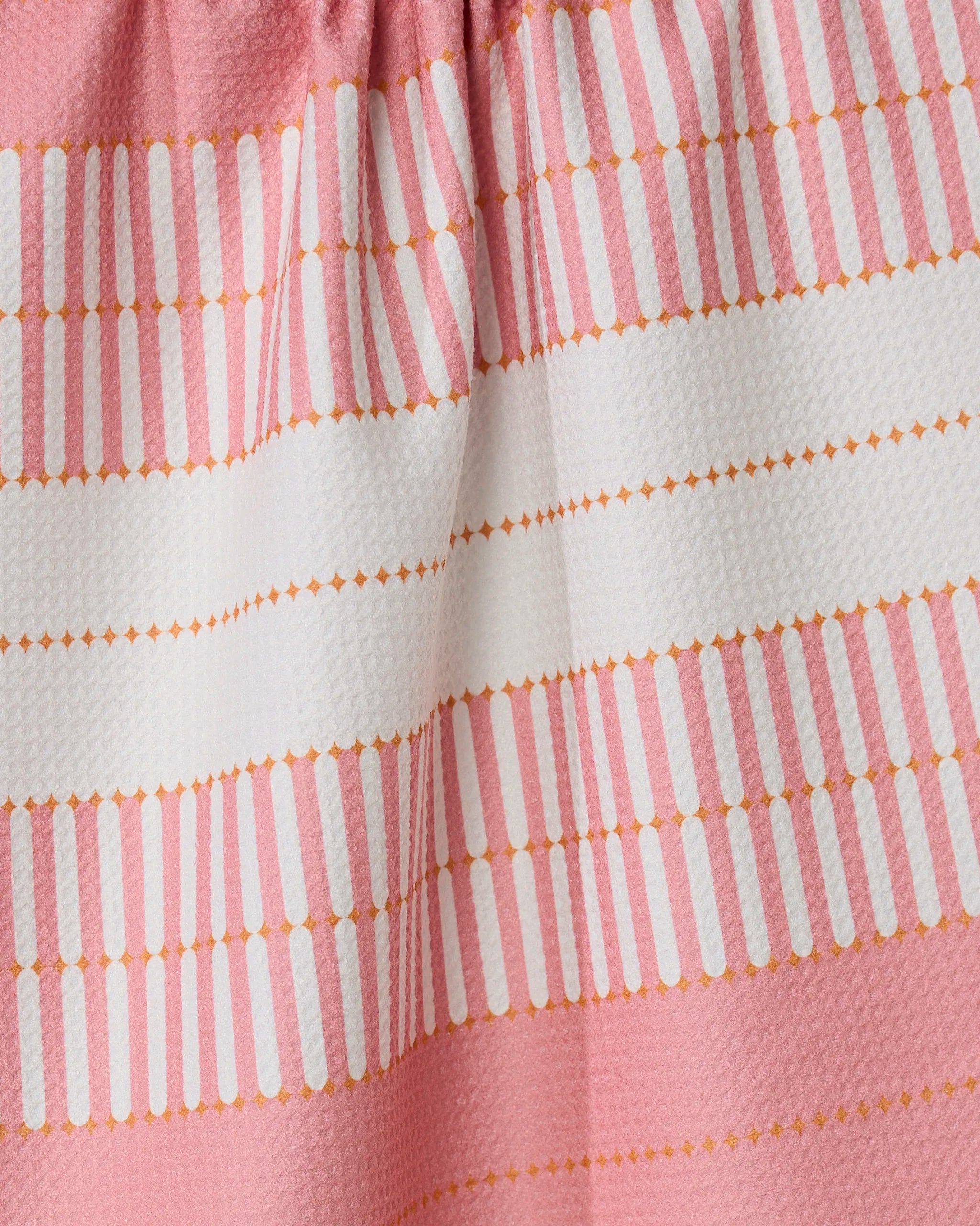 A close-up of the GEOMETRY Bâton Rose, a pink ultra-absorbent towel with white horizontal stripes and dotted yellow lines, showing its textured surface and gathered folds near the top.