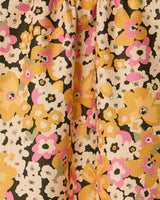 A close-up of the GEOMETRY Beloved Bunch kitchen towel, an eco-friendly option with a vibrant floral pattern in yellow, pink, white, and black on a light background. The fabric features a textured surface and gentle gathered folds.