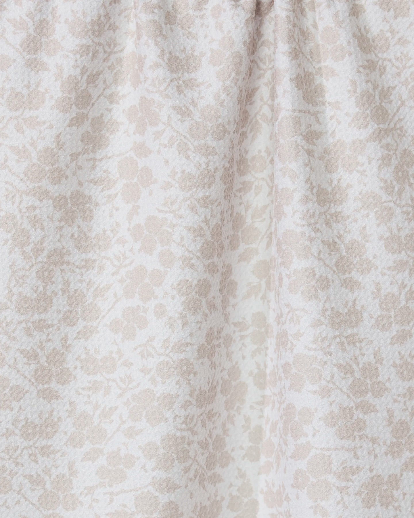A close-up of GEOMETRYs Bettys Buds, a light beige tea towel made from recycled materials, featuring a subtle floral pattern and gentle gathered folds near the top.