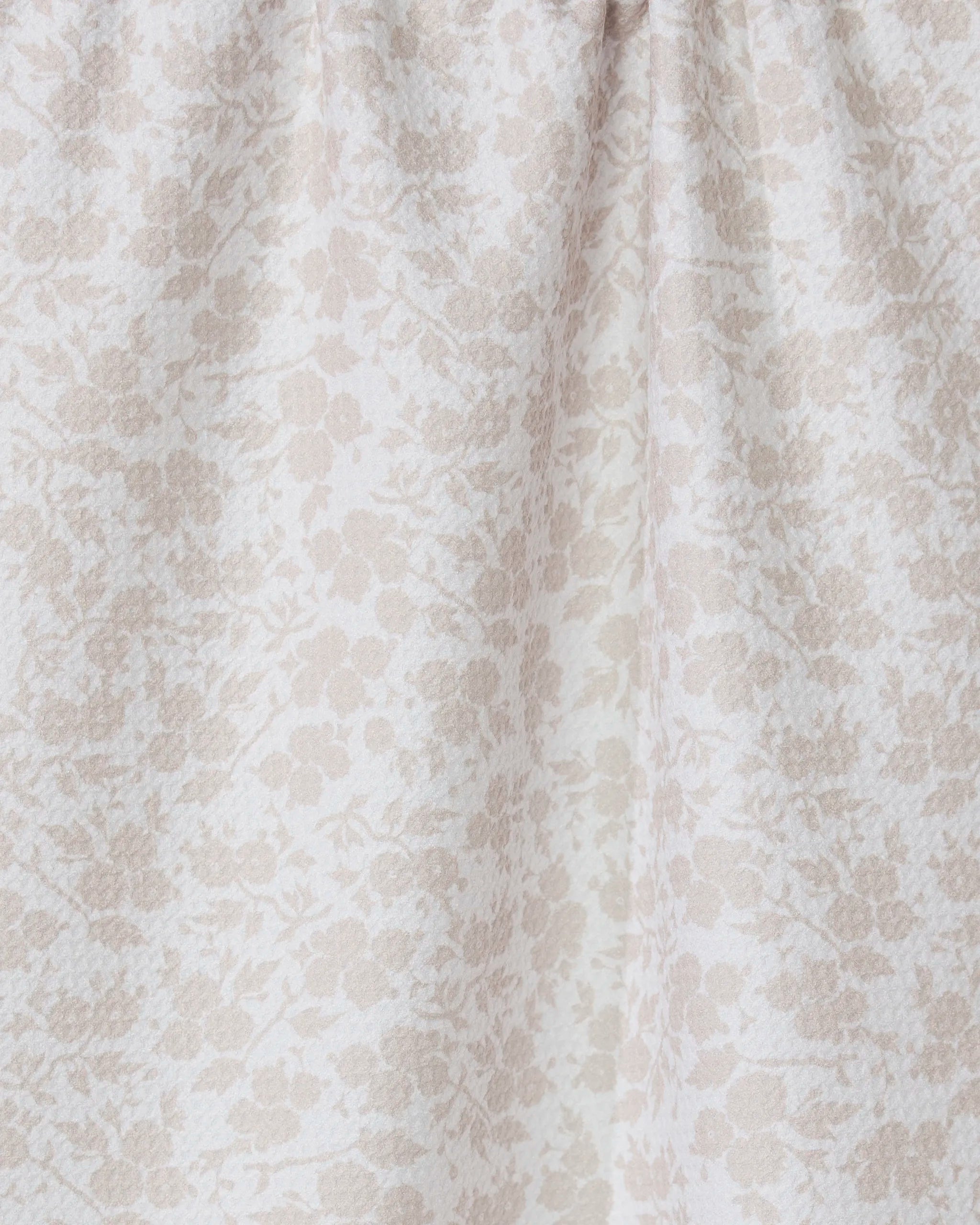 A close-up of GEOMETRYs Bettys Buds, a light beige tea towel made from recycled materials, featuring a subtle floral pattern and gentle gathered folds near the top.