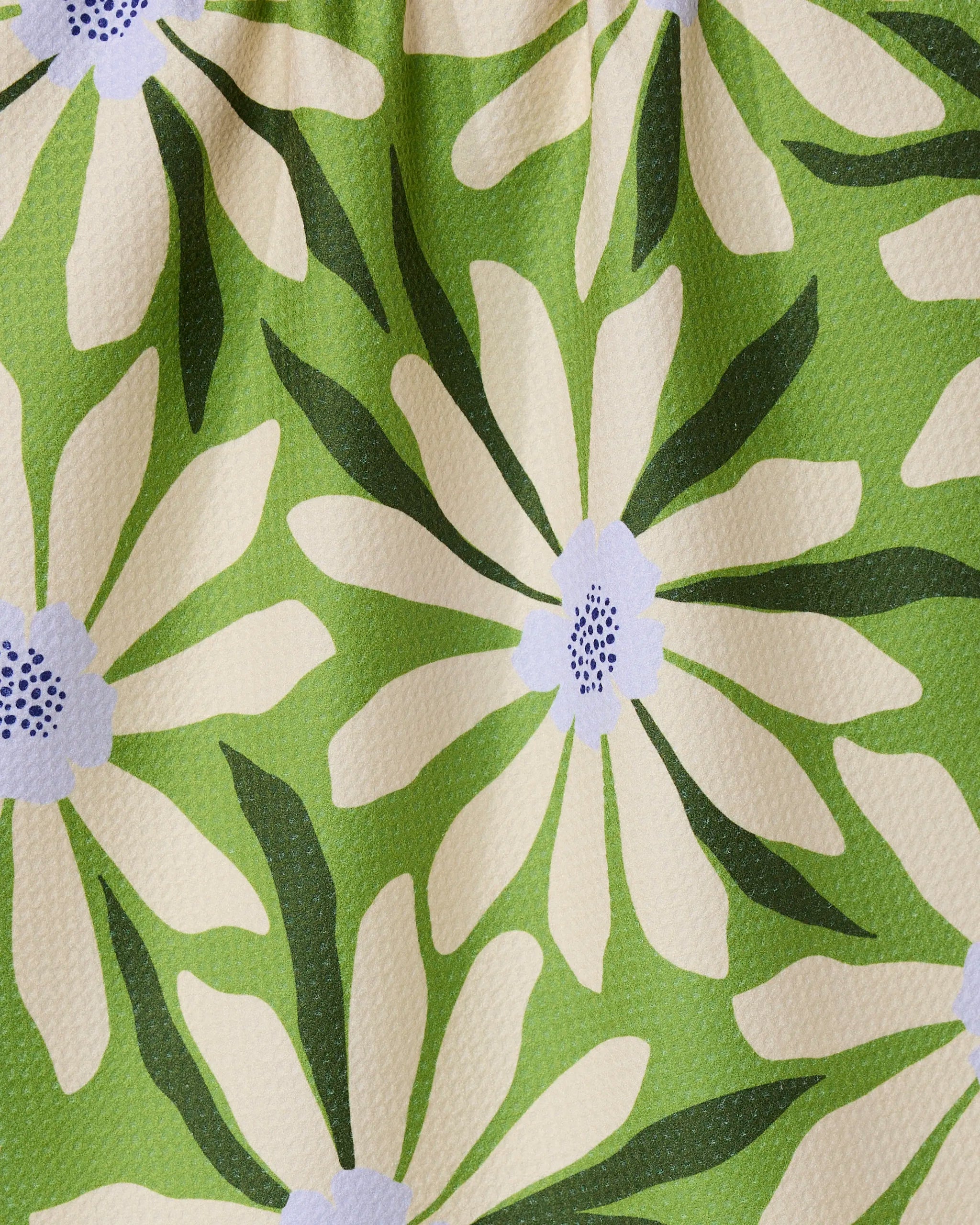 The GEOMETRY Bliss and Bloom tea towel features large cream daisies and dark green leaves on light green, crafted from quick-drying recycled materials with a subtle textured look.
