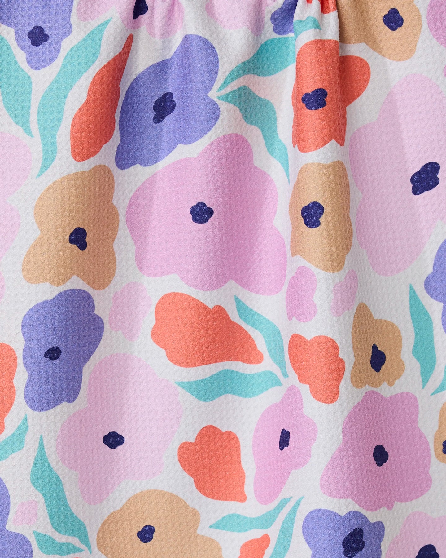 A close-up of GEOMETRYs Blossoming Love tea towel, made from recycled materials, featuring a colorful floral pattern with pink, orange, purple, and tan flowers with dark centers and green leaves on a textured white background.