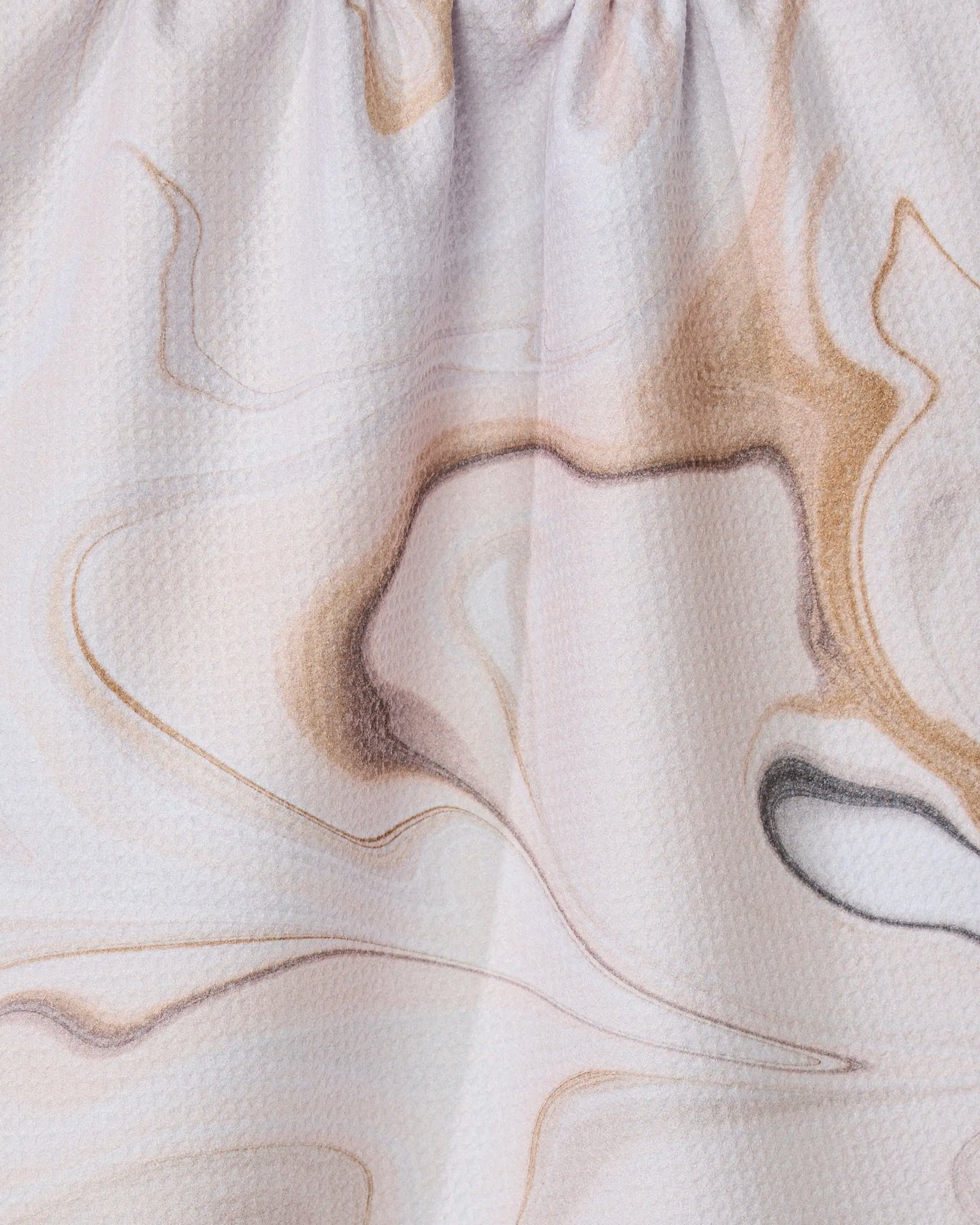 Close-up of Choco by GEOMETRY, a textured fabric crafted from recycled materials with a soft, swirling marble pattern in beige, brown, and light pink. The fabric is gently gathered at the top.