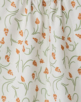 The GEOMETRY Crayon Floral tea towel features white textured fabric with orange floral clusters and green curving stems and leaves. Slightly gathered at the top, it offers style, function, and a light, airy look.