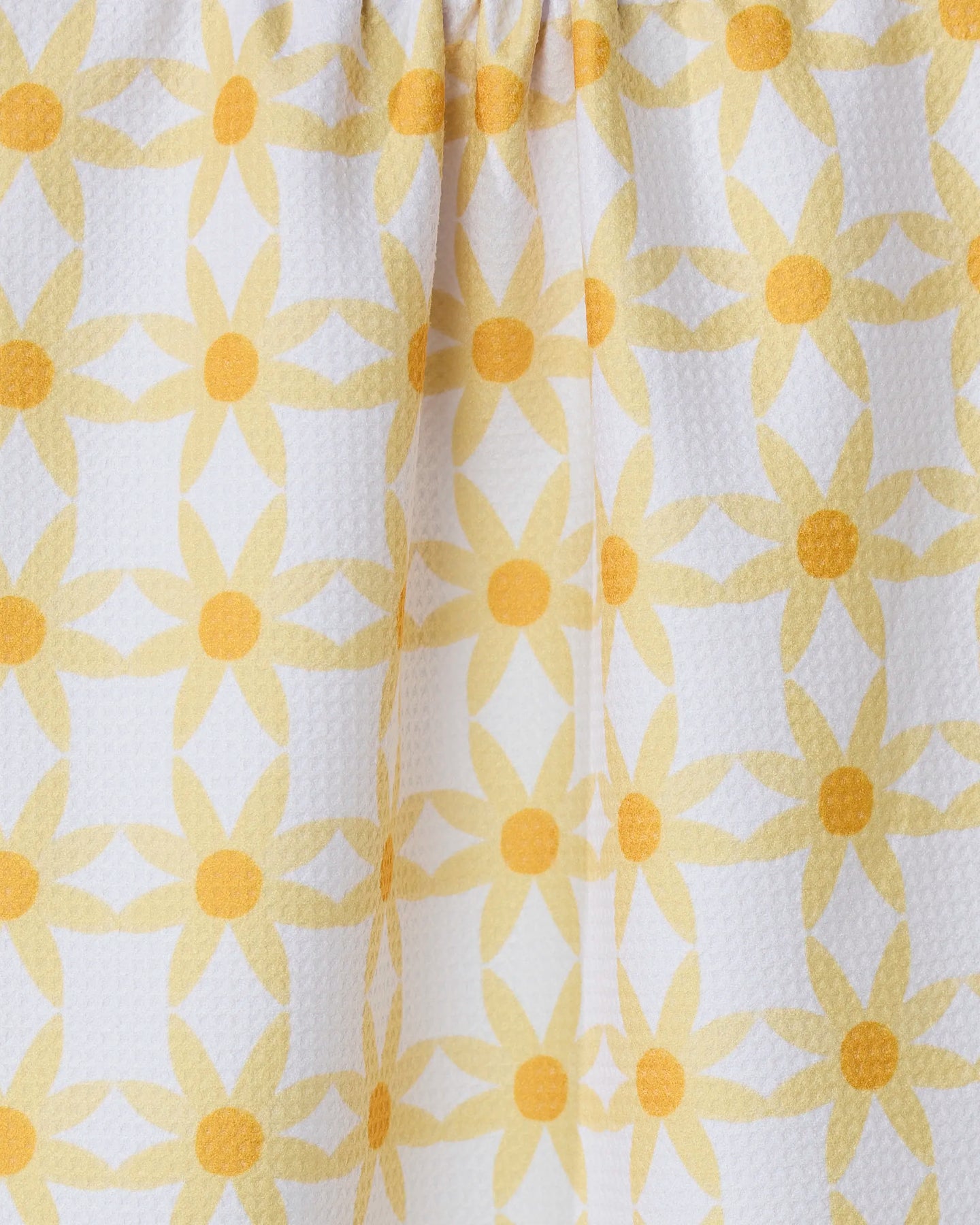 Close-up of the GEOMETRY Daisies kitchen tea towel, featuring a repeating yellow floral pattern with circular centers on white, ultra-absorbent textured fabric and gentle folds.