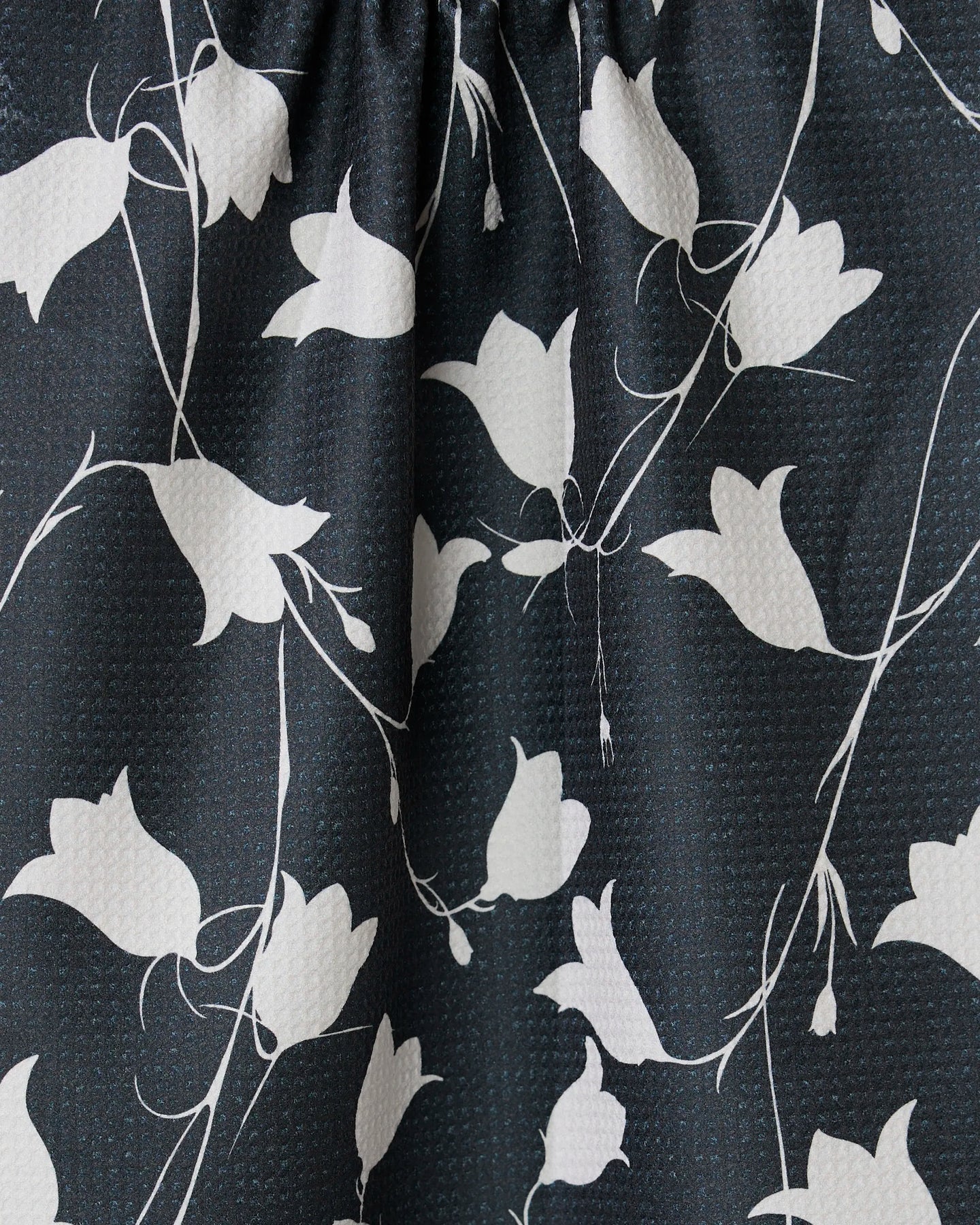 Close-up of GEOMETRYs Dancing Dark Flora tea towel, showcasing black fabric with a textured surface and a white pattern of abstract floral designs and slender vines.