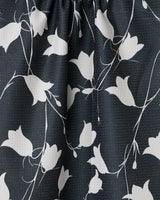 Close-up of GEOMETRYs Dancing Dark Flora tea towel, showcasing black fabric with a textured surface and a white pattern of abstract floral designs and slender vines.