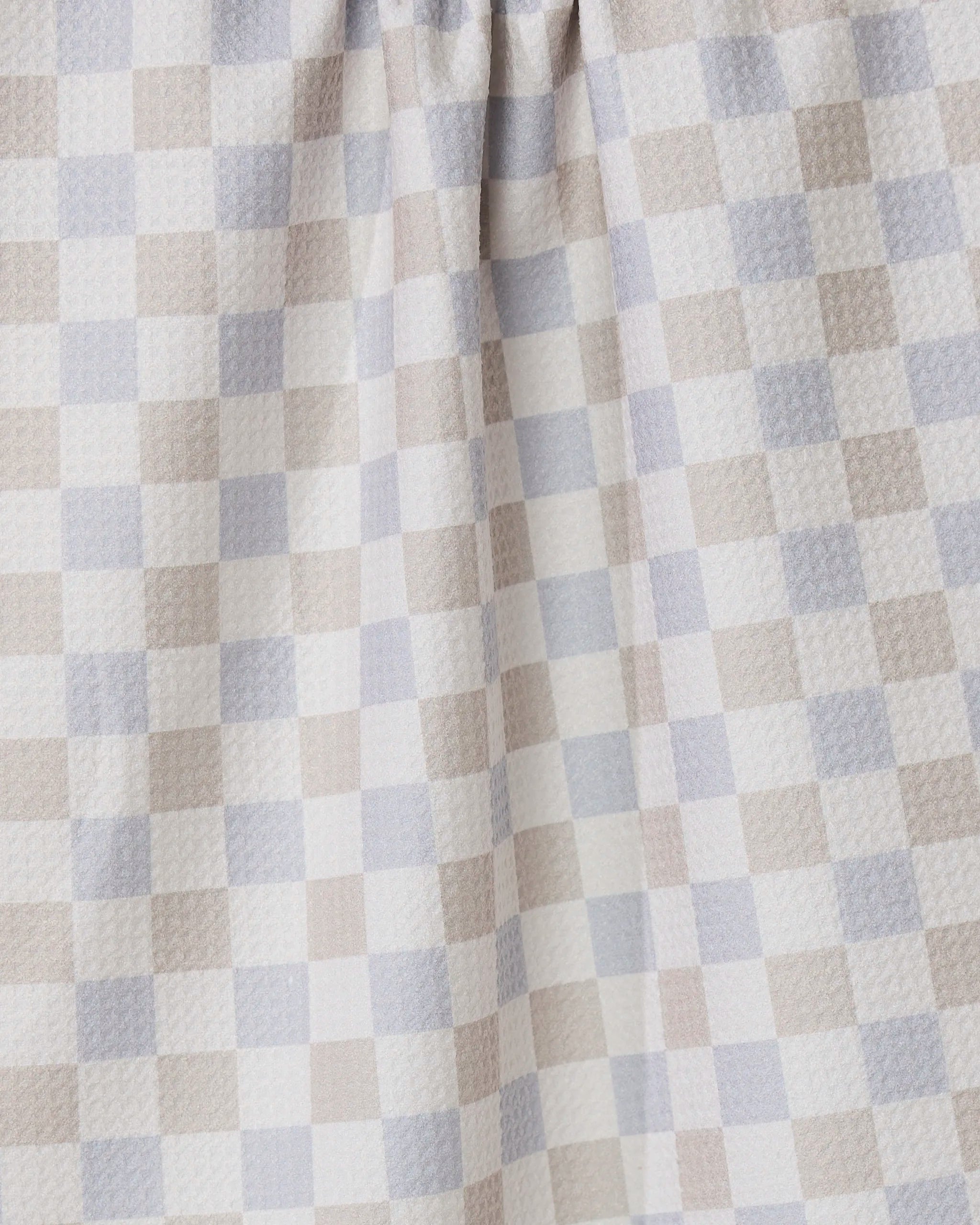 A close-up of the Danse Neutre quick-drying towel by GEOMETRY, featuring a checkered pattern in soft beige, light gray, and white. The fabric is gently gathered at the top, highlighting its texture and folds.